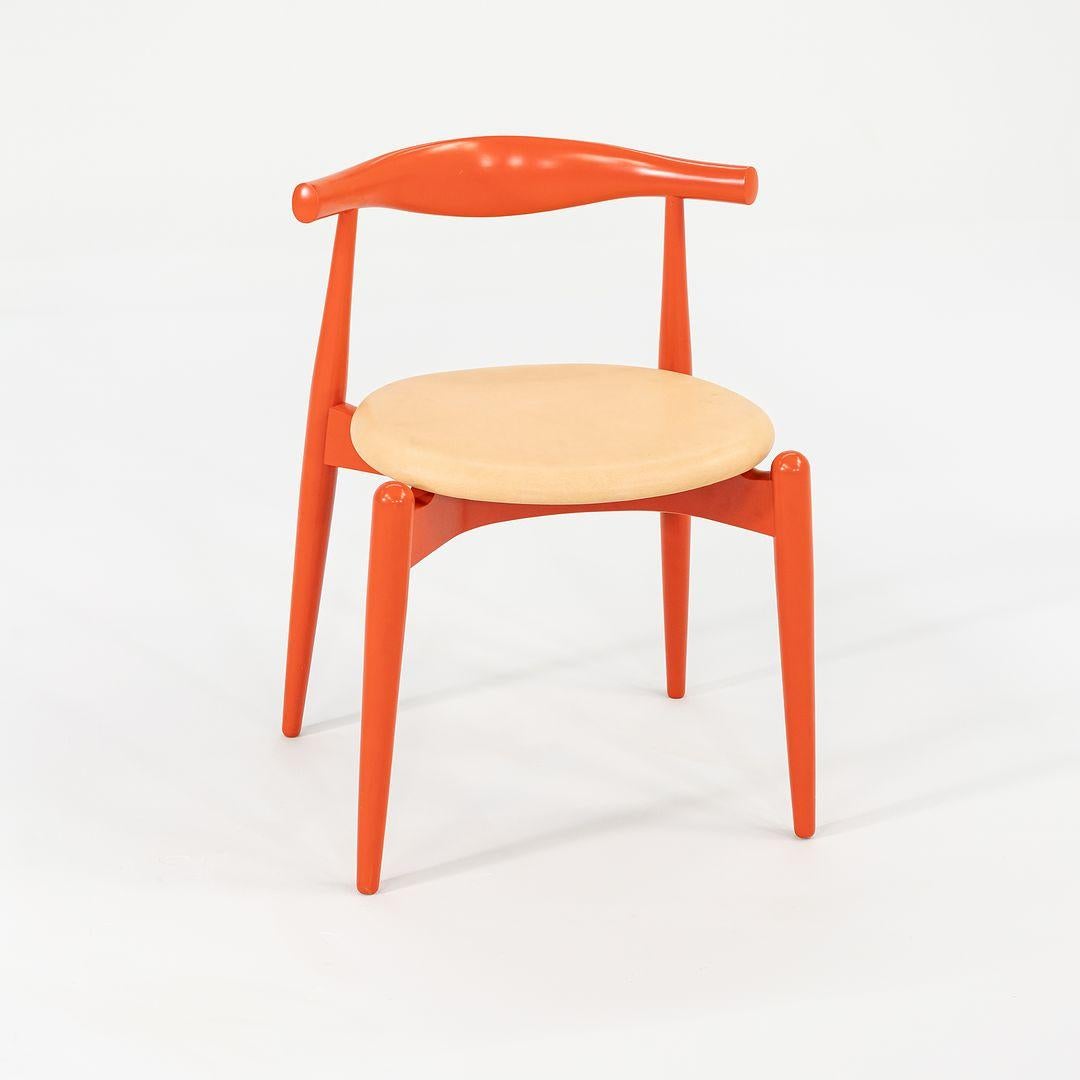 This is a CH20 Elbow Dining Chair made with a bright orange wood frame and yellow leather seat. The chair, designed by Hans Wegner and produced by Carl Hansen & Son in Denmark, dates to circa 2022 and is guaranteed as authentic. Condition is
