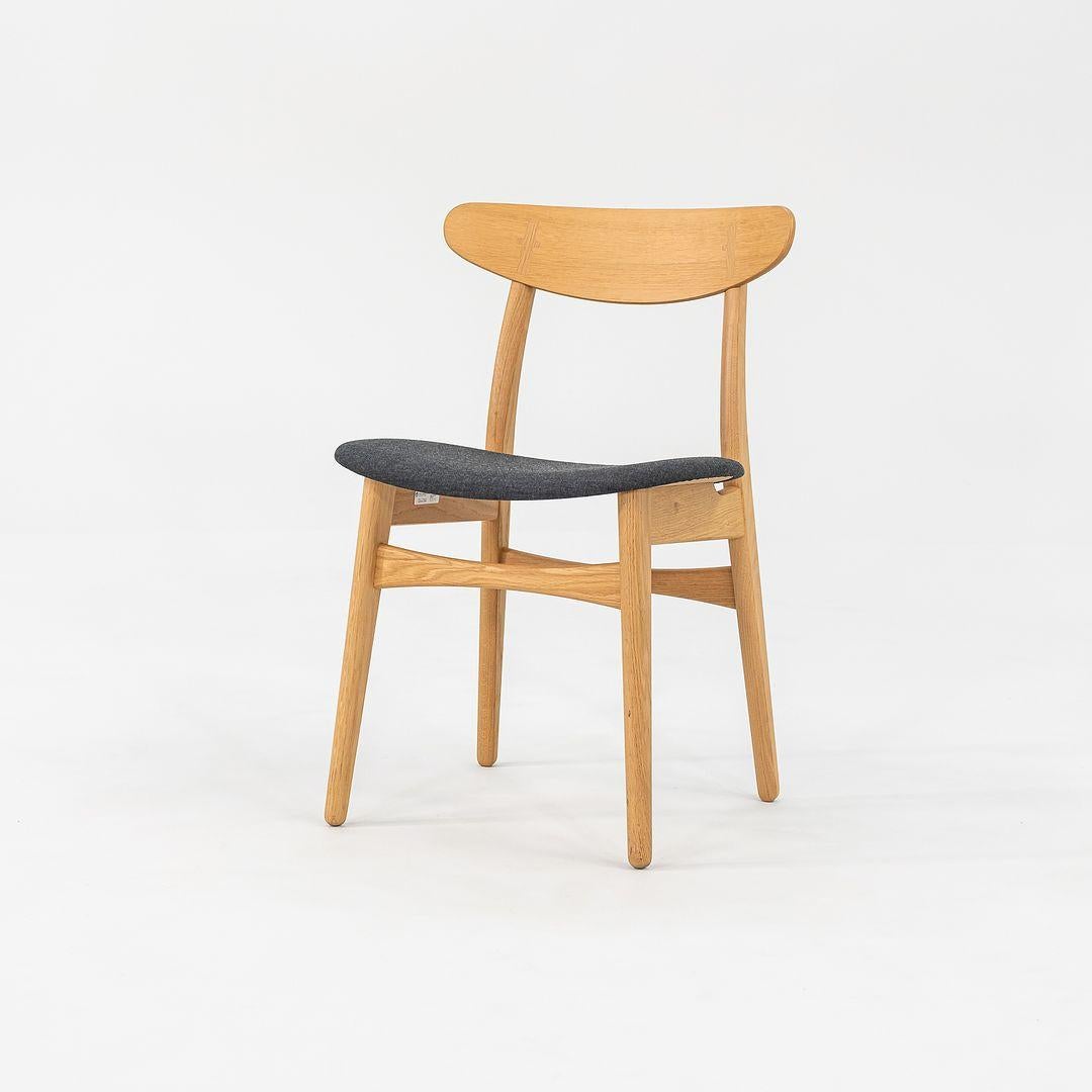 Questa sedia da pranzo CH30P è realizzata con una solida struttura in Oak e un tessuto intrecciato grigio scuro. La sedia, disegnata da Hans Wegner e prodotta da Carl Hansen & Son in Danimarca, risale al 2022 circa ed è garantita come autentica. La