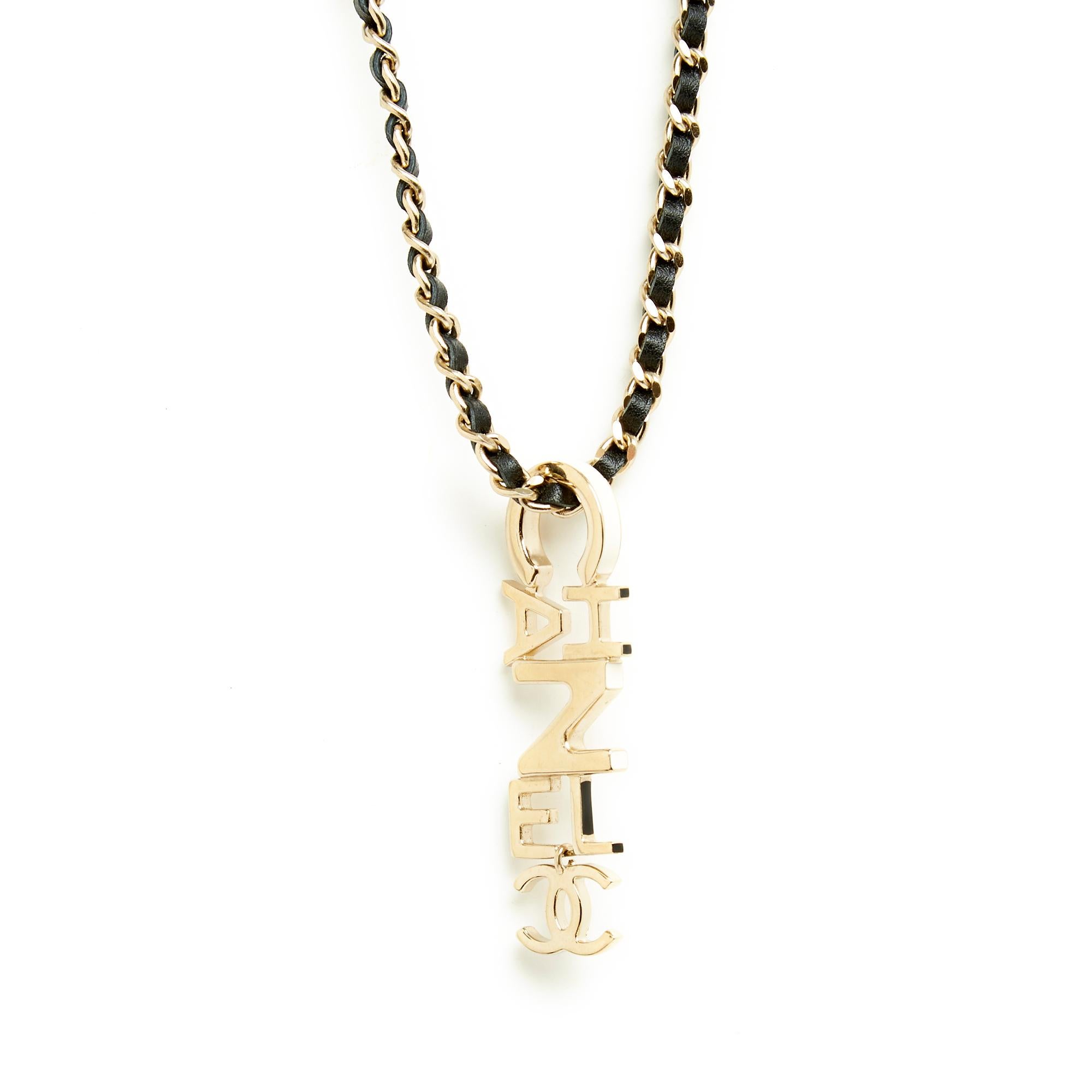 Chanel long necklace or belt collection 2022 in lightly gilded metal composed of a chain interwoven with black leather and a pendant with the letters and logo of Chanel enameled in black or ecru on the edge, closing with a carabiner on a chain