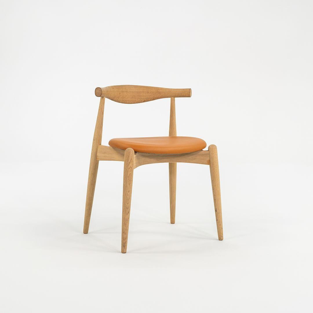 Questa è una sedia da pranzo a gomito CH20 con struttura in rovere massiccio e seduta in pelle color caramello. La sedia, disegnata da Hans Wegner e prodotta da Carl Hansen & Son in Danimarca, risale al 2022 circa ed è garantita come autentica. Le