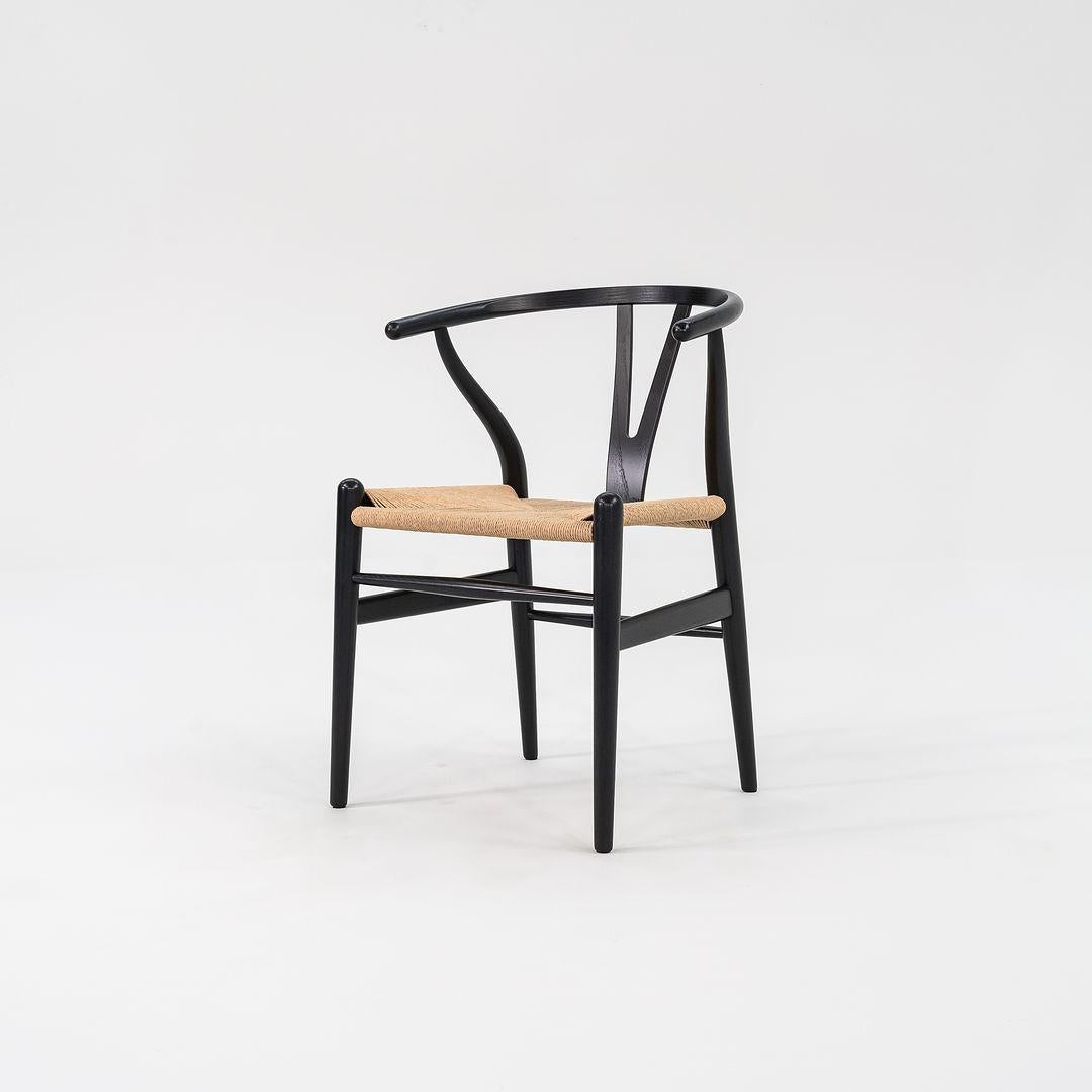 Questa è una sedia da pranzo Wishbone CH24 con struttura in Oak verniciata di nero e seduta in corda di carta naturale. Disegnata da Hans Wegner e prodotta da Carl Hansen & Son in Danimarca, la sedia risale al 2022 circa ed è garantita come