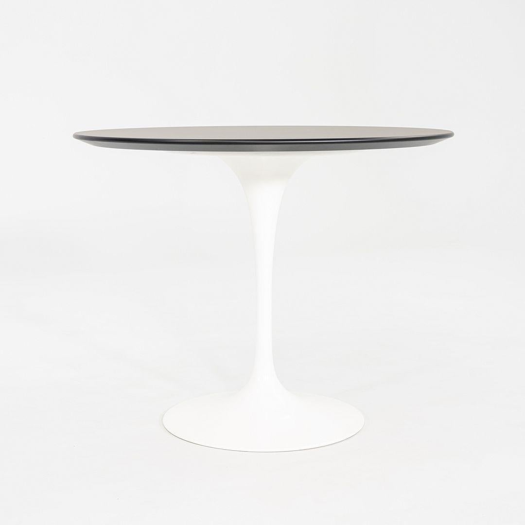 This is a Tulip Dining Table, originally designed by Eero Saarinen for Knoll in 1956. This particular example was produced in the United States by Knoll in 2023. The table features a black laminate top with a beveled edge and a signature cast