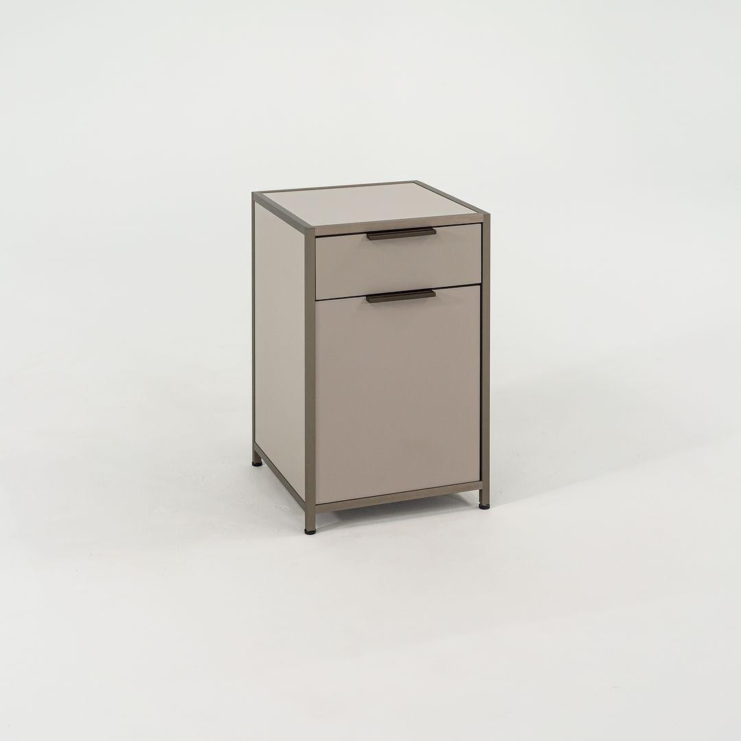 Listed for sale is a pair of small Dita nightstands with one drawer and one door. One door opens left and the other opens right. The chest is made of tan lacquered wood panels and an anodized aluminum frame. The color is noted as Argile / Bronze.
