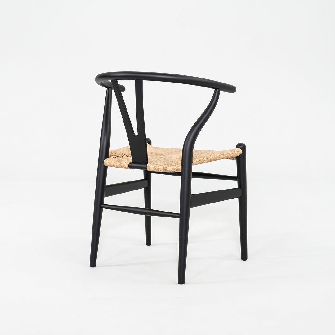 This is a set of four CH24 Wishbone dining chairs, originally designed by Hans J. Wegner in 1949. These particular examples were produced by Carl Hansen in Denmark C. 2023. The chairs are made with a solid beech frame, painted black with a natural
