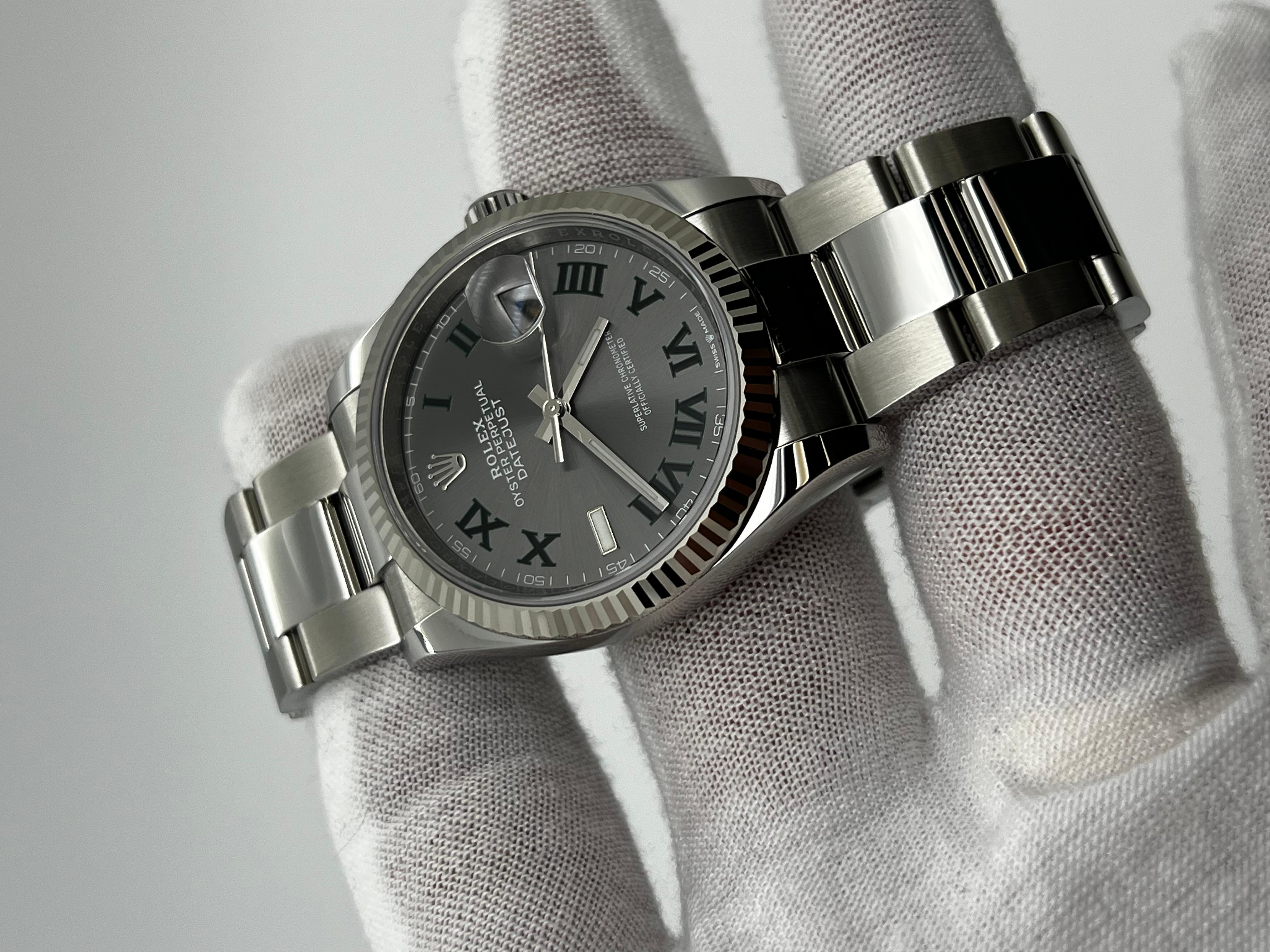 Style Number: 126234
Serial: JT332***
Year: 2024
Model: Rolex Datejust 
Case Material: Stainless Steel 
Band: Stainless Steel 
Bezel: 18K White Gold Fluted
Dial: Slate Wimbledon
Face: Sapphire Crystal 
Case Size: 36mm 
Includes: 
-Rolex Box &