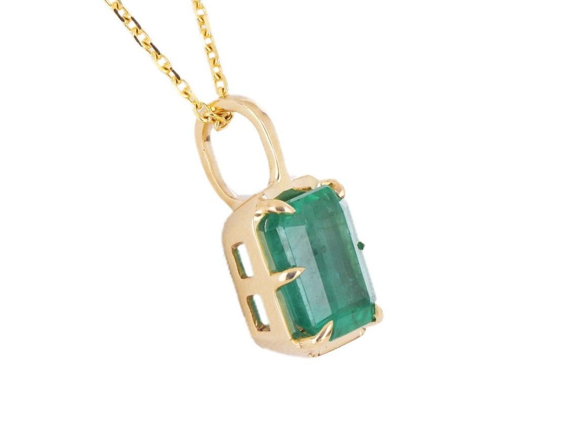 Displayed is a natural emerald Georgian styled solitaire pendant in 14K yellow gold. This gorgeous solitaire pendant carries an earth-mined emerald in a prong setting. Fully faceted, this gemstone showcases excellent shine. The emerald has good
