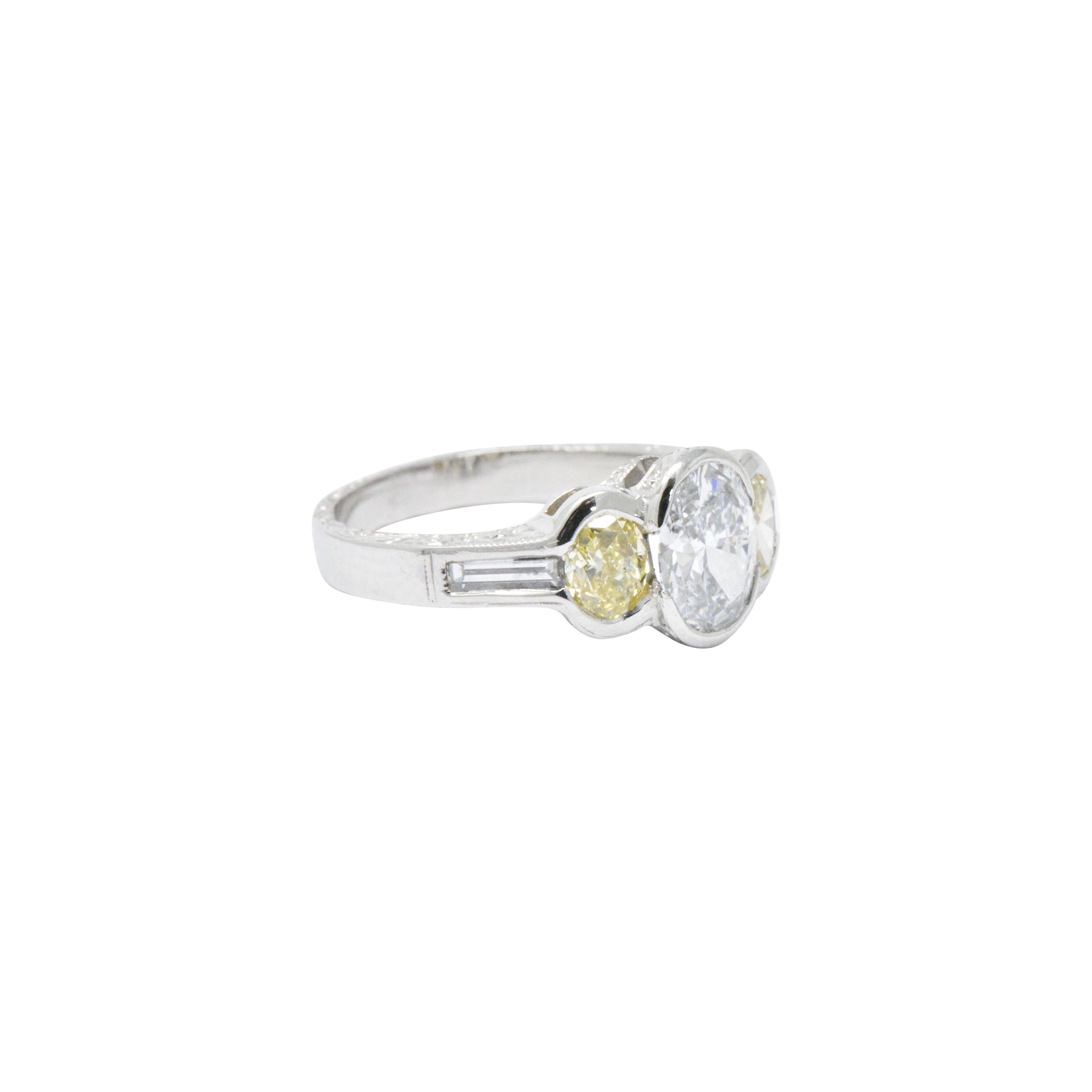 Centering a brilliant oval cut diamond weighing 1.02 carats, E color, VS2 clarity and accompanied by GIA Diamond Grading Report, in a classy partial bezel setting

Flanked by two fancy yellow oval brilliant cut diamonds weighing 0.76 carats total,