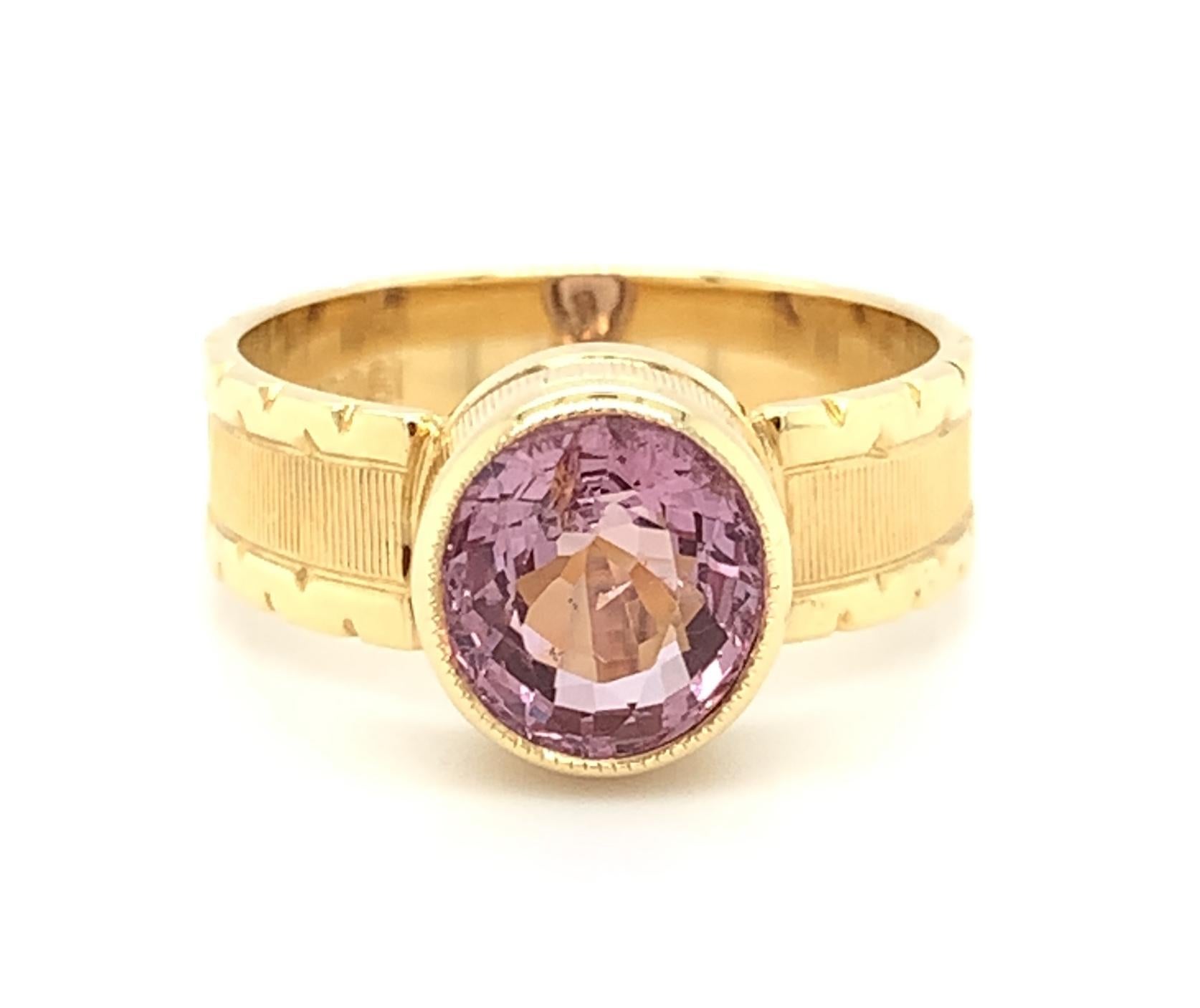 A sparkling, 2.03 carat rose pink spinel is highlighted in this beautifully handmade 18k yellow gold band ring. Intricate details have been added to every angle of this masterfully created ring, from the top and sides of the bezel to the sides of