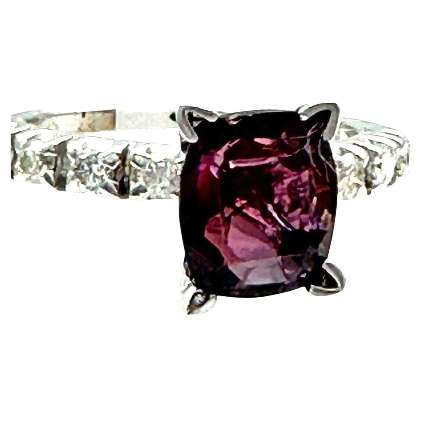 The 14-karat white gold ring showcases a rare, modified oval cushion cut reddish-purple sapphire solitaire diamond ring. The sapphire measures 8.05-7.07 x 3.95 mm and weighs 2.03 carats. The color of the sapphire is purple with a reddish tone, and