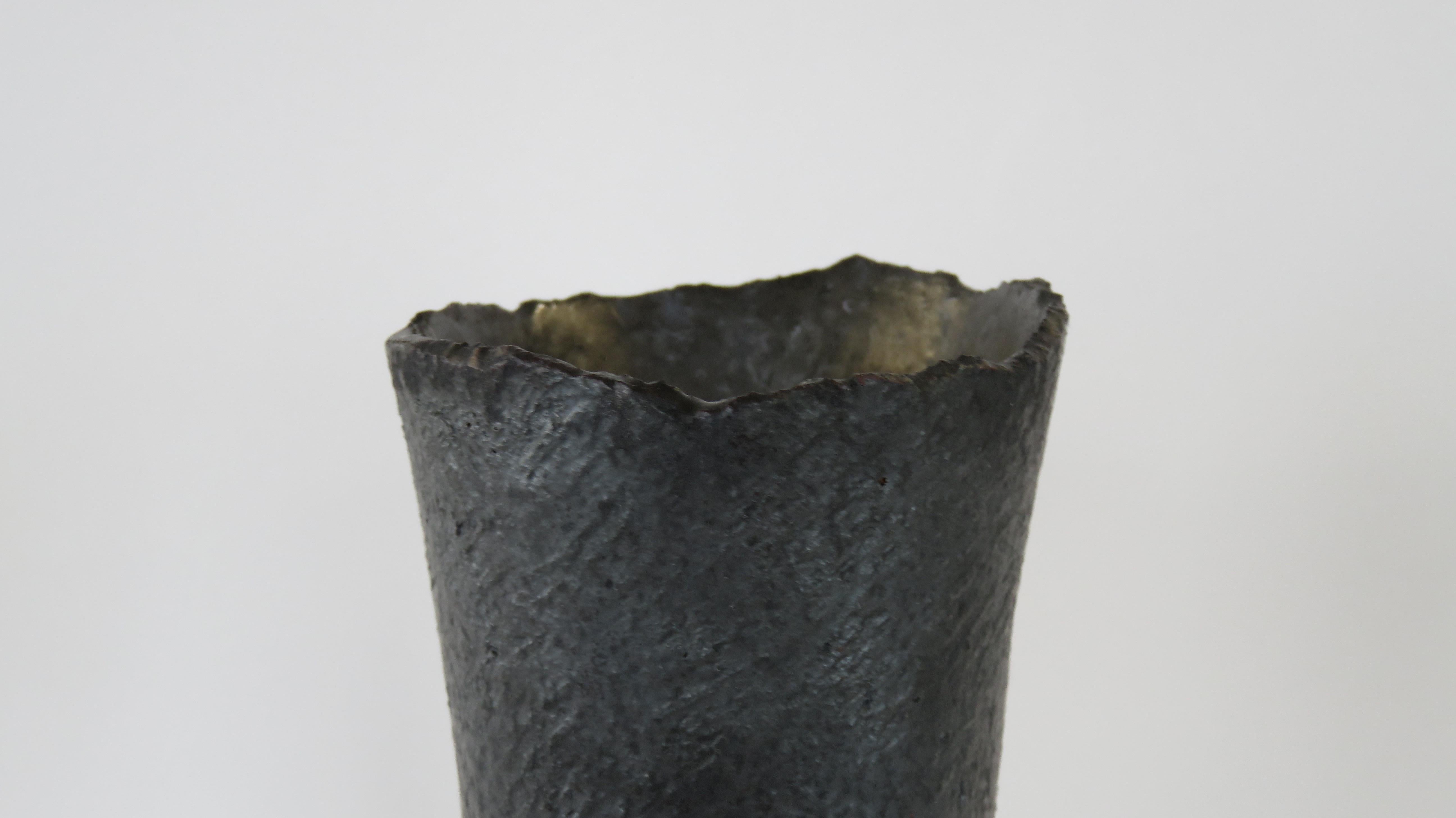These tall ceramic vases in a metallic black glaze over stoneware are weighted on the bottom for tall floral arrangements or branches. Each surface is scraped to show the texture and tone of the clay, with varying bases or knobby edges. The top rims