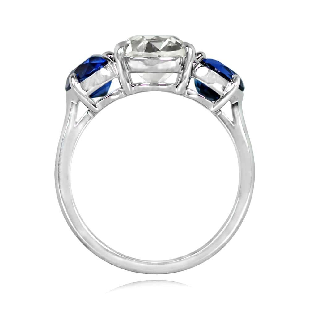 This three-stone ring showcases a 2.03-carat old European cut diamond with J color and VS2 clarity at the center. The diamond is flanked by two pear-shaped natural sapphires with a combined weight of 2.04 carats, all set in prongs. The mounting is