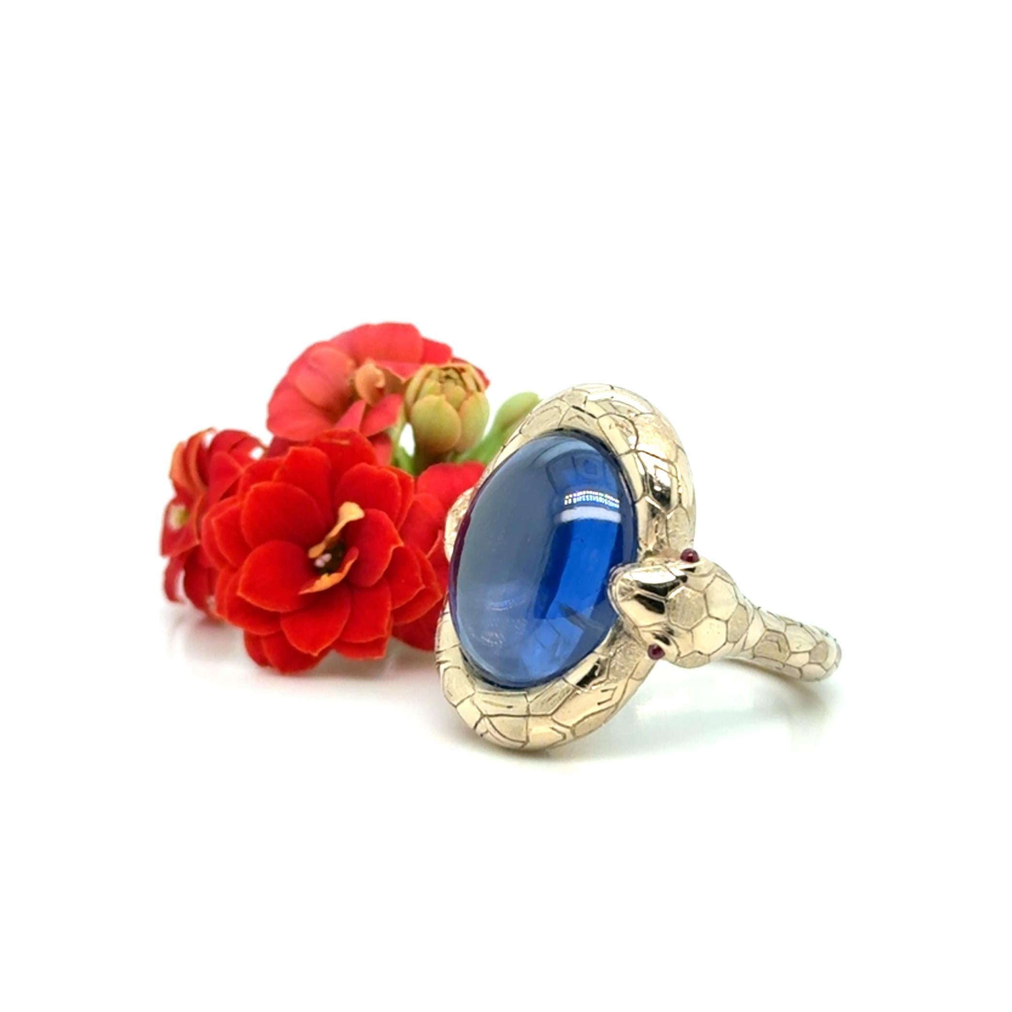A sapphire ring in 18K gold, featuring a double cabochon-cut 20.43ct untreated natural sapphire from Sri Lanka. The ring is designed in the shape of a snake, with smaller cabochon-cut rubies set as eyes. The inside of the ring is adorned with a