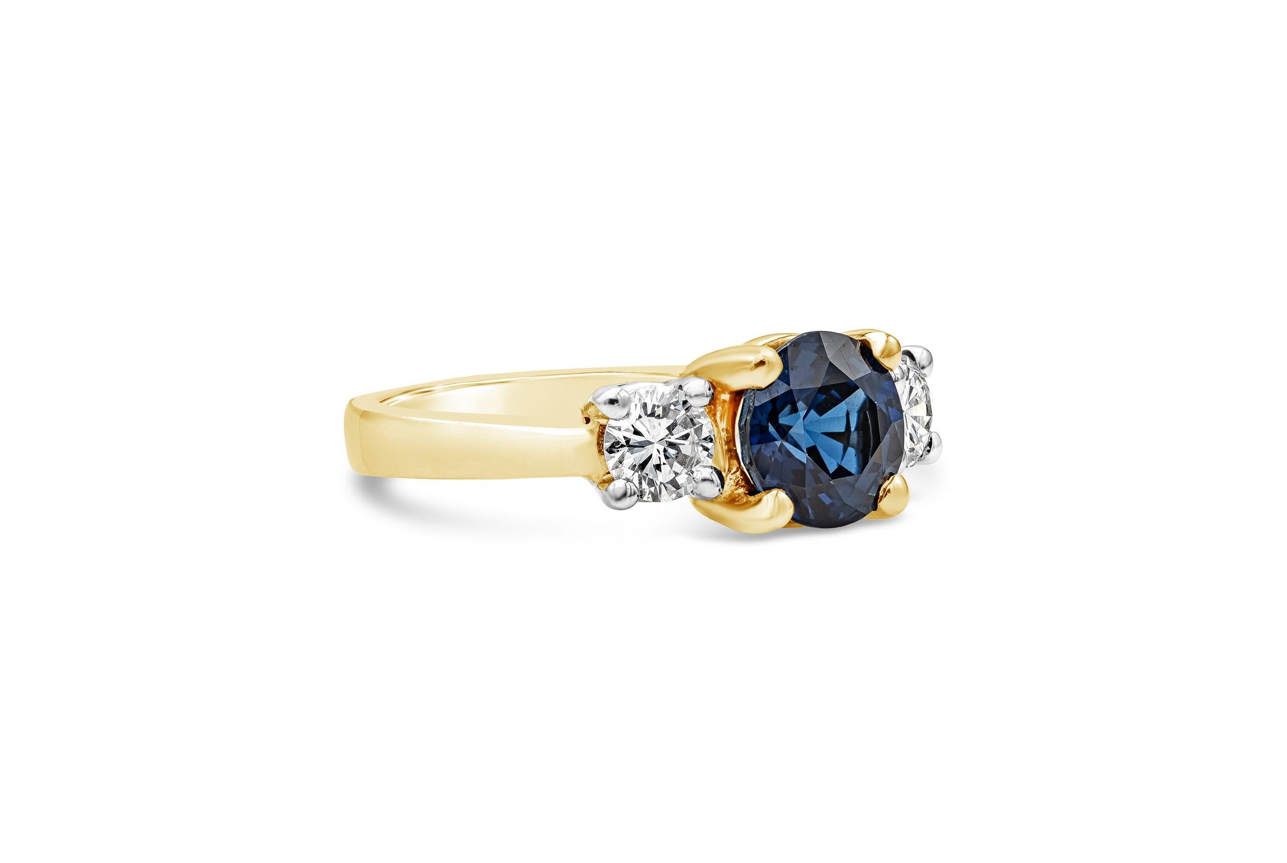 A gorgeous three stone gemstone engagement ring showcasing a round blue sapphire center stone weighing 2.05 carat total, elegantly flanked by a single round cut diamond on each side weighing 0.60 carats total, set in a timeless four prong setting