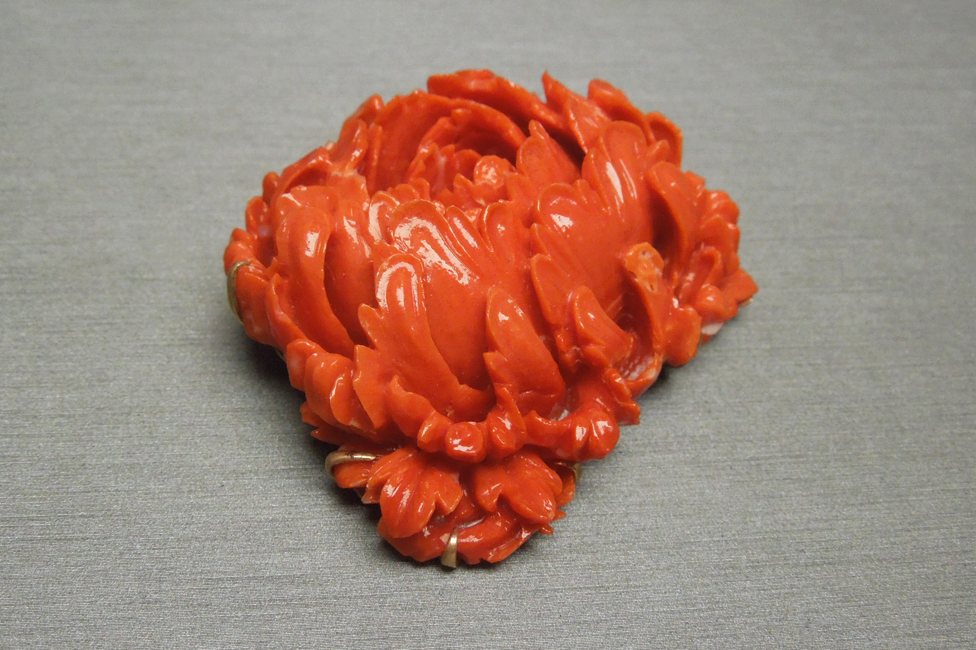 This period Victorian brooch features a single Natural Ox Blood Red Coral intricately Hand Carved into a Chrysanthemum flower weighing in at 205.00 carats, secured in a 9-prong electronically tested 10KT Gold frame with complementary pierced out