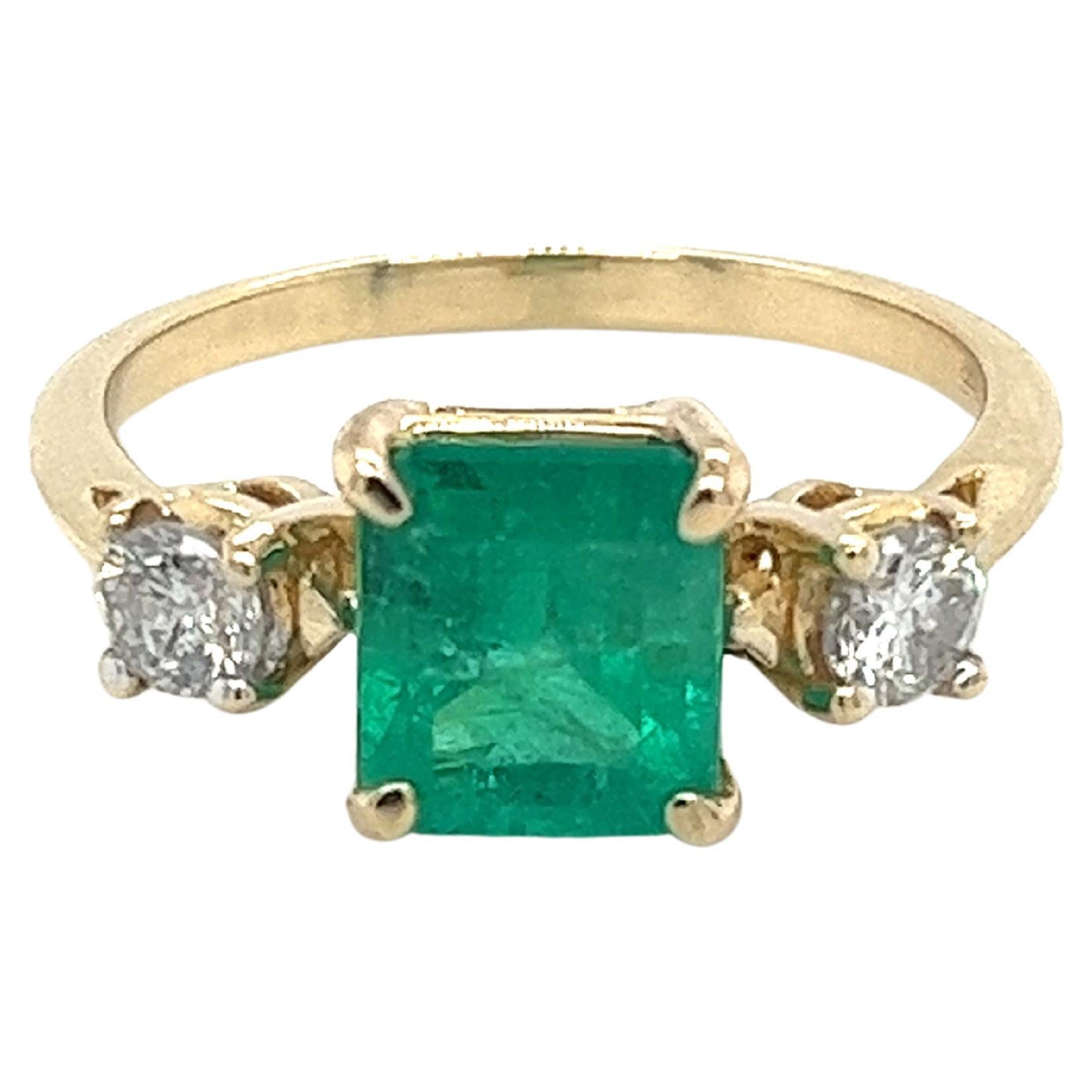 Natural 2.05 carat Colombian emerald and diamond three stone ring in 14k solid yellow gold. Featuring an elegantly thin band that accentuates the center stones. A dainty setting with a center stone of pristine quality. The emerald is vibrant and