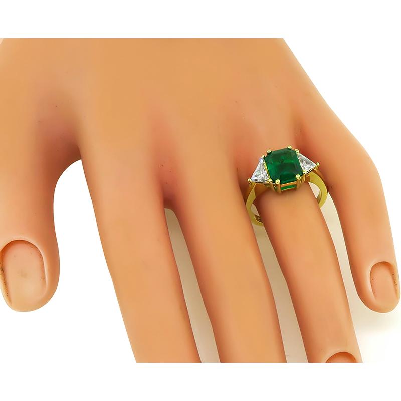This is an amazing 18k yellow gold ring. The ring is centered with a lovely emerald cut Colombian emerald that weighs approximately 2.05ct. The center stone is accentuated by sparkling trilliant cut diamonds that weigh approximately 0.75ct. The