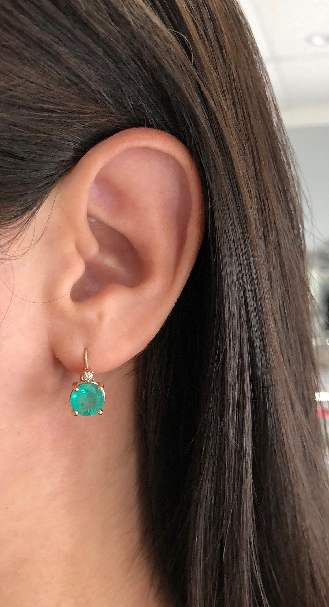 A beautiful pair of round Colombian emerald and diamond lever back earrings made in 14K rose gold. The chic pair of lever back earrings feature bluish-green, natural Colombian Emerald rounds. The emeralds have beautiful eye clarity and are simply