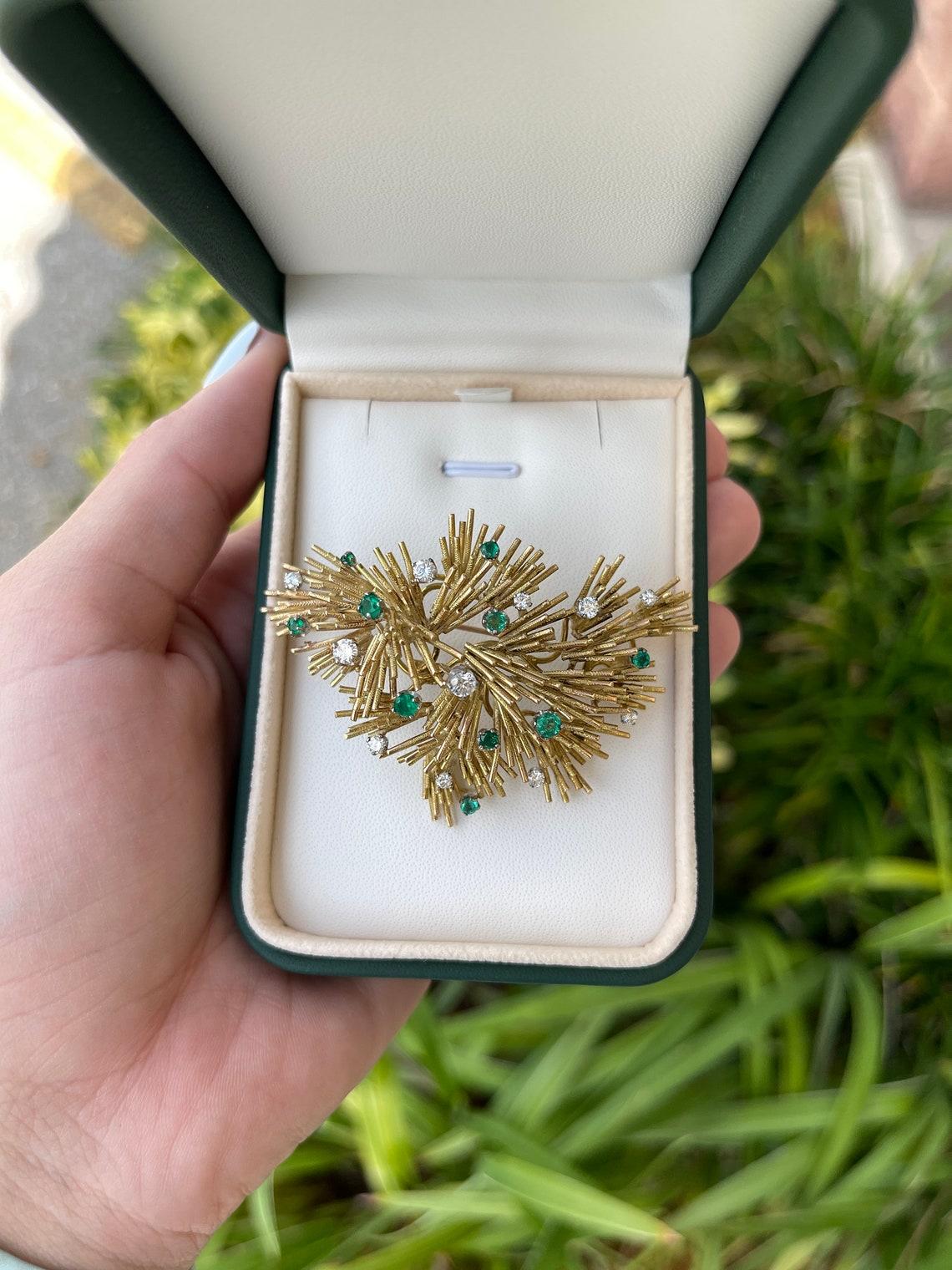 Diese außergewöhnliche Brosche aus 18-karätigem Gold wurde von unserem Meisterjuwelier in exquisiter Handarbeit gefertigt. Elegant präsentieren sich elf runde Brillanten mit einem Gesamtgewicht von 1,08 ct und zehn sattgrüne kolumbianische Smaragde