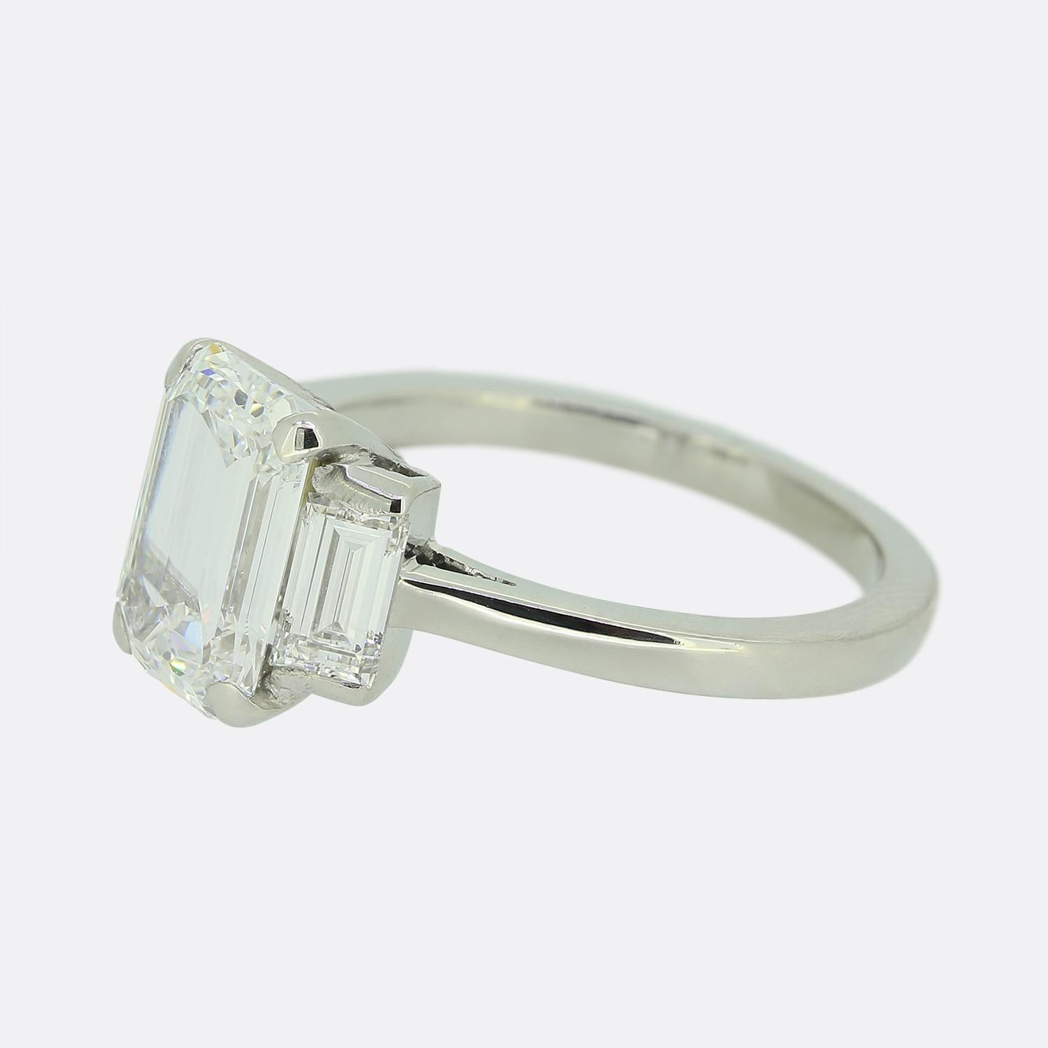 Hier haben wir einen eleganten und raffinierten Verlobungsring mit einem spektakulären Diamanten im Smaragdschliff als Herzstück. Dieser makellose weiße Diamant wird von zwei Diamanten im Baguetteschliff flankiert, die seine Brillanz verstärken. Die