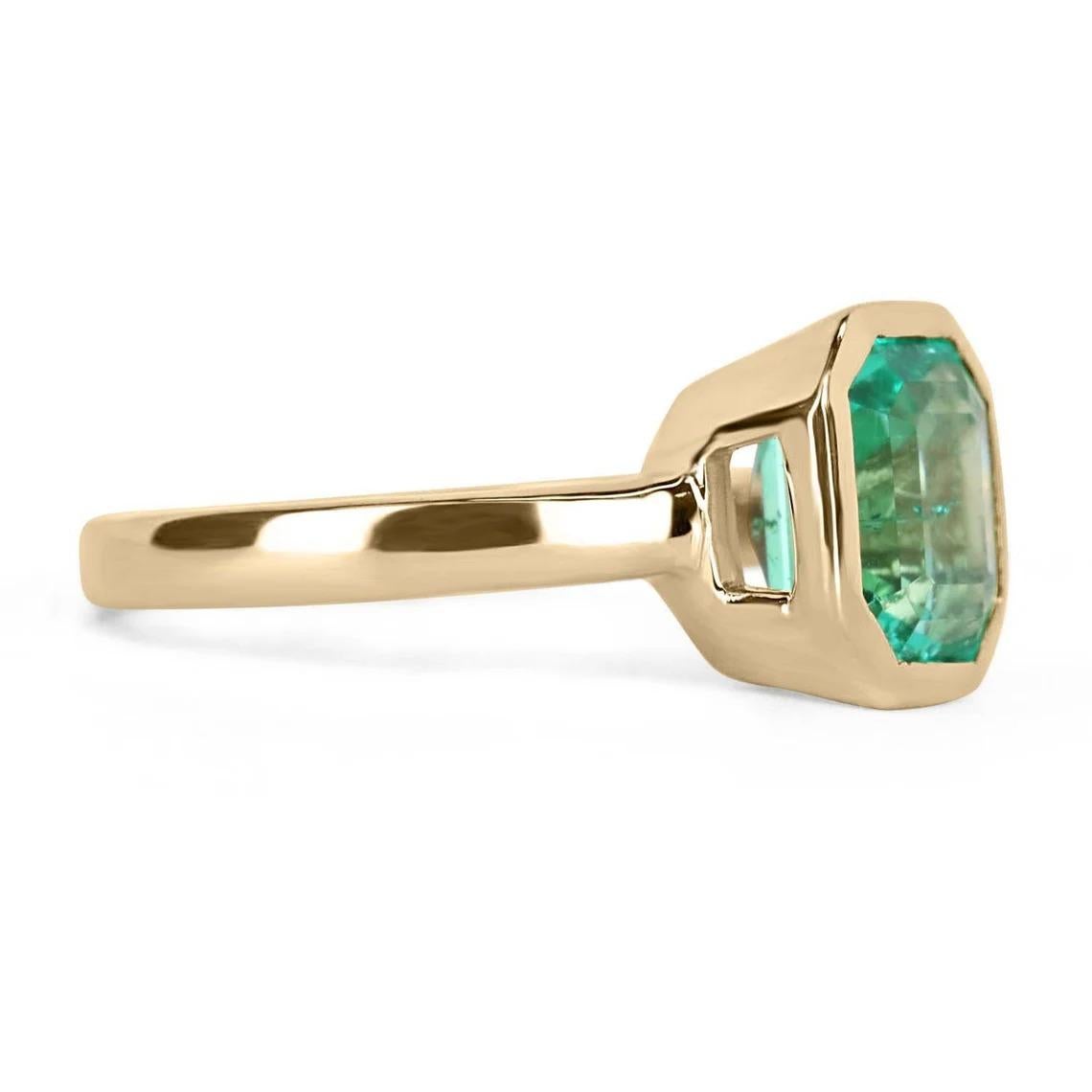 Displayed is a bluish-green Colombian emerald, solitaire, emerald-cut bezel ring in 18K yellow gold. This gorgeous solitaire ring carries a full 2.06-carat emerald in a sleek bezel setting. The emerald has very good clarity and luster, with minor