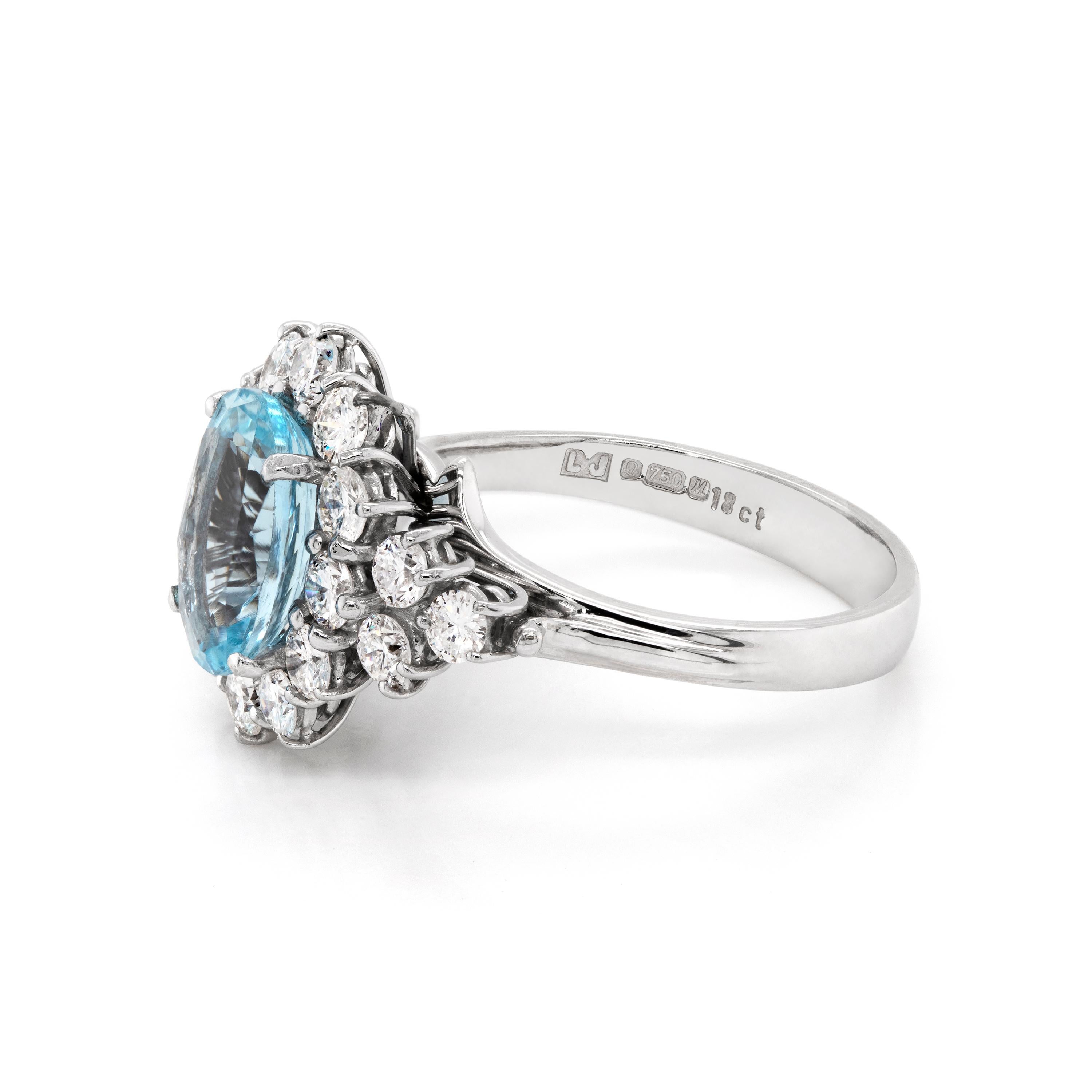 This exquisite engagement ring features a vibrant oval shaped aquamarine weighing 2.07ct set in an open back, four claw setting. The aquamarine is beautifully surrounded by 12 round brilliant cut diamonds, with an added cluster of three diamonds
