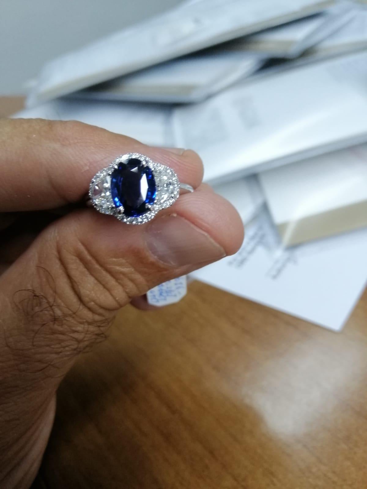 Dieser elegante und klassische Ring zeigt einen natürlichen und unerhitzten ovalen blauen Ceylon-Saphir von 2,07 Karat, der von zwei Halbmond-Diamanten (0,64 Karat) von Osten nach Westen eingerahmt und von einem Diamantenkranz umgeben ist, der den