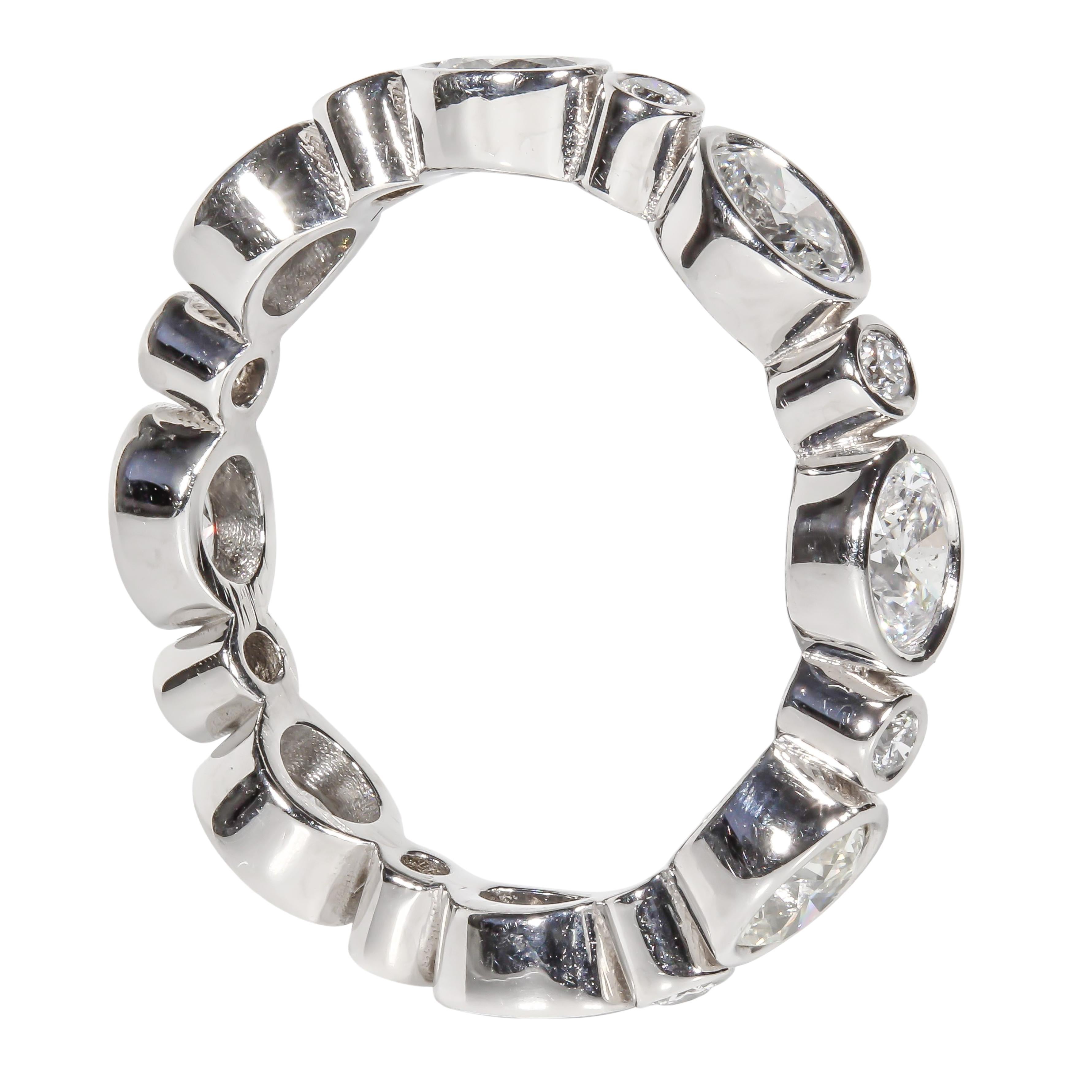 14 karat white gold eternity band ring containing 1.85 carats of bezel set oval brilliant and 0.22 carats of round brilliant natural diamonds. The color and clarity grades of the diamonds have been graded internally as F-G, VS1-SI1 for the oval