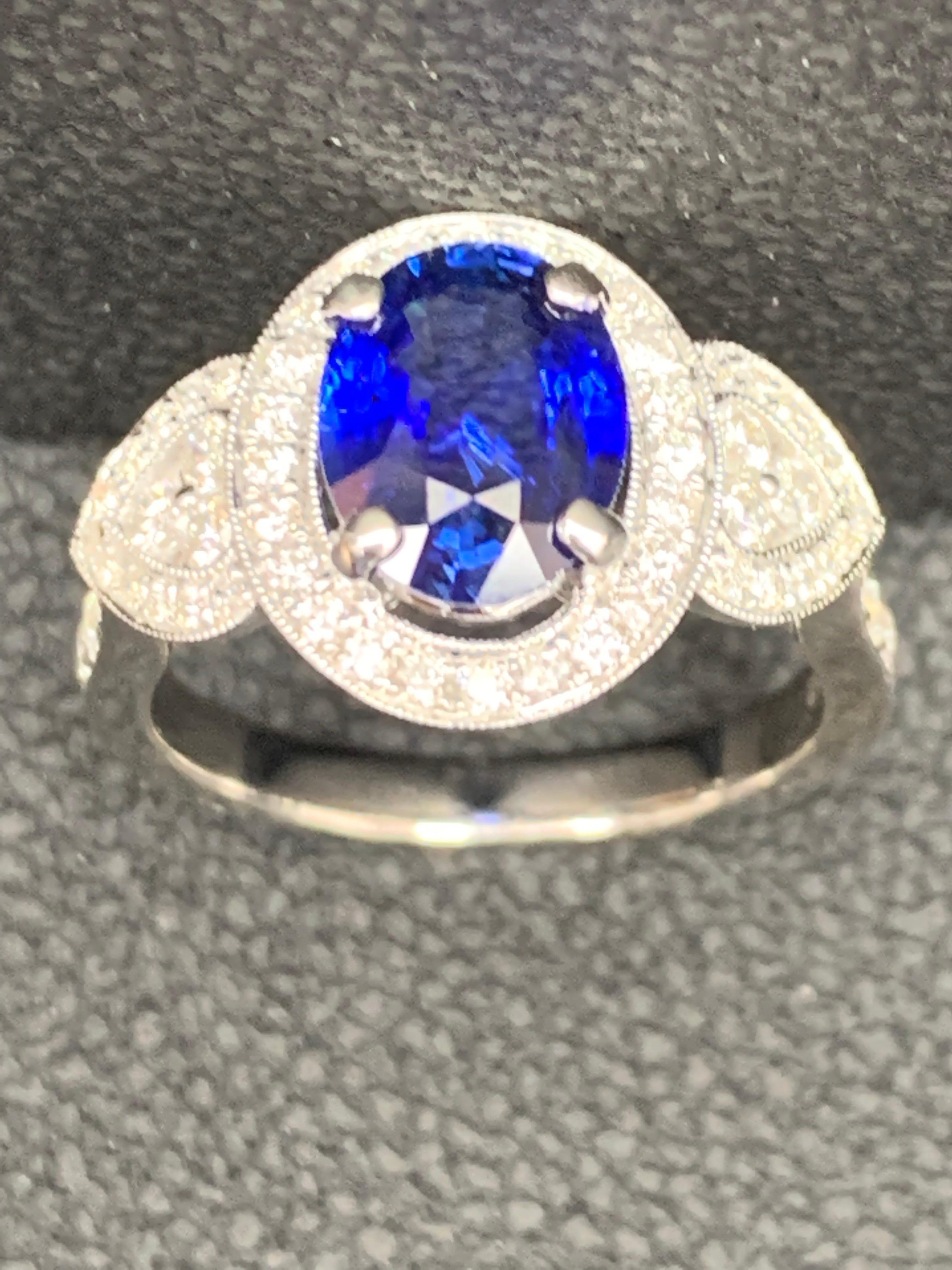 This engagement ring features a 2.08 carat oval cut blue sapphire set in 4 prongs made with 18 Carats white gold. The center stone is flanked by round brilliant diamonds. A floating halo of melee diamonds accent the side diamonds for a unique