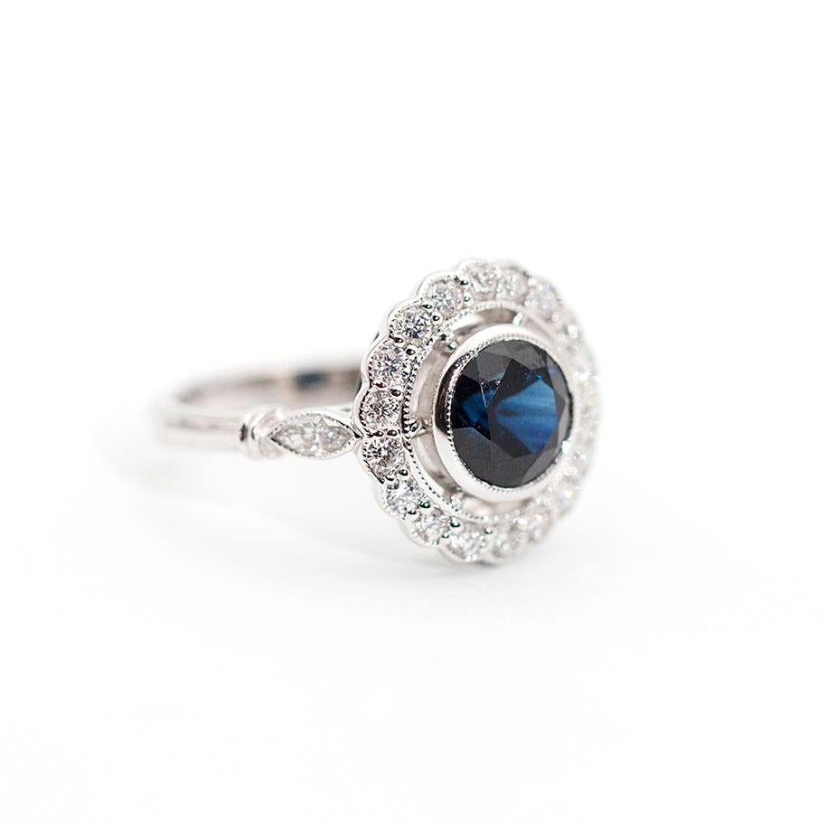 This darling art deco inspired ring is forged in 18 carat white gold and features an alluring 2.09 carat round natural deep blue Australian sapphire encompassed by a total of 0.59 carats of diamonds in a pretty vintage halo bead set with bright