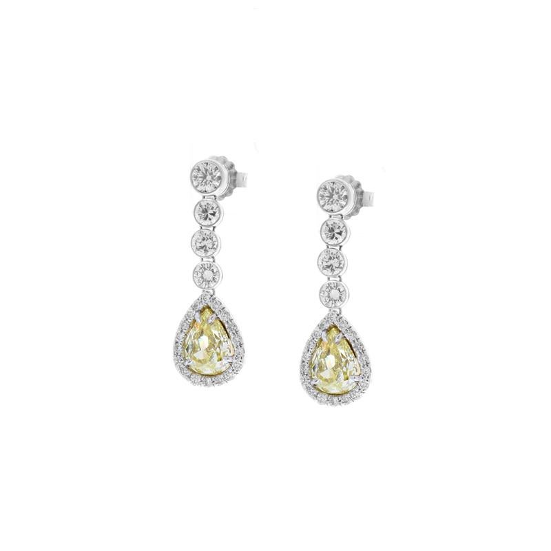 These luxurious diamond drop earrings are absolutely breathtaking! They feature dazzling white diamonds set in a linear design that drop down to illuminating pear shaped natural fancy yellow diamond centers. The fancy yellow diamonds are lemon