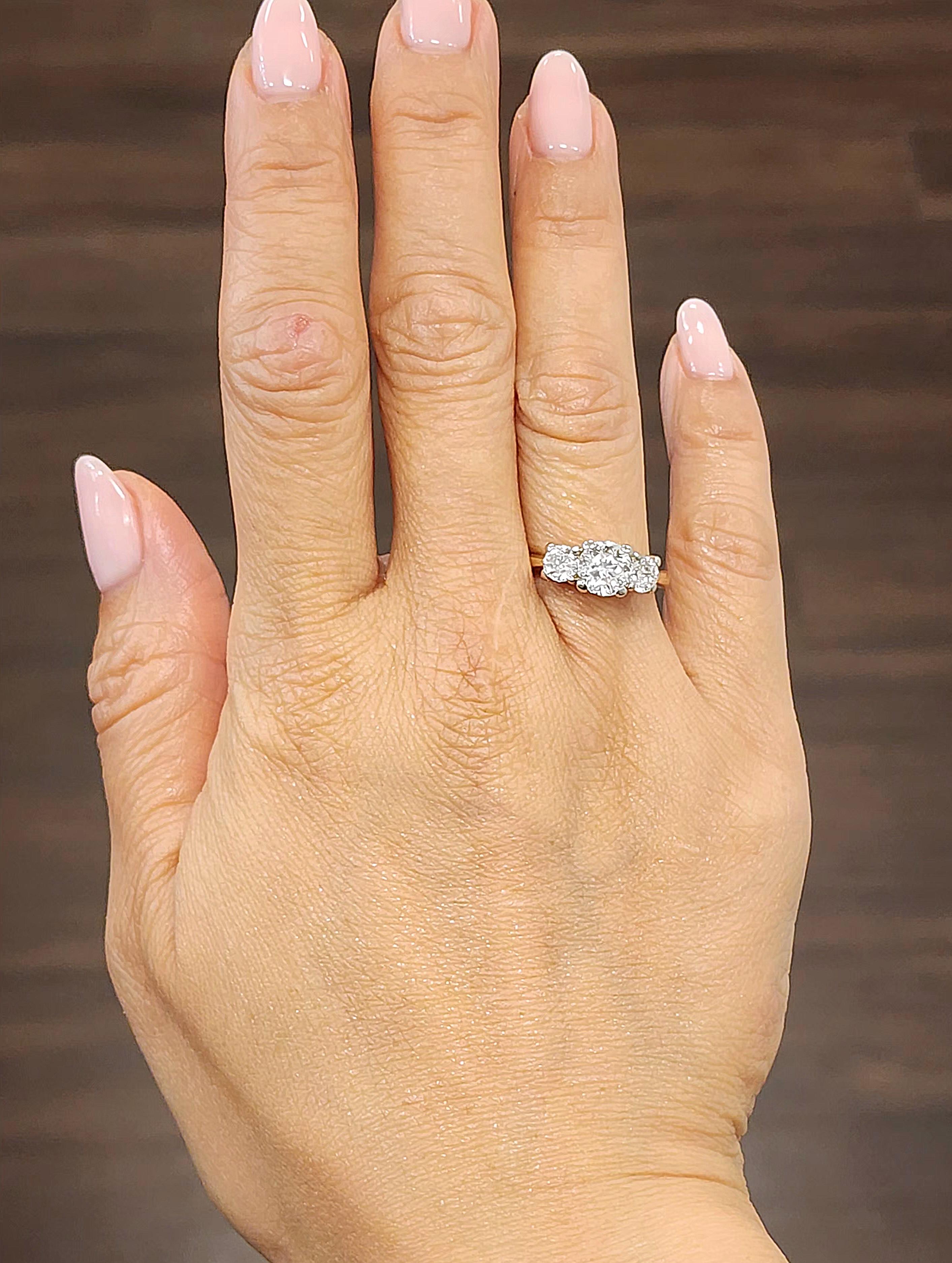 Este exquisito anillo de compromiso de tres piedras tiene como pieza central un impresionante diamante redondo de 1,27 ct. El diamante es de color F y claridad VVS2, e irradia un tono blanco brillante. Flanqueando la piedra central hay dos diamantes