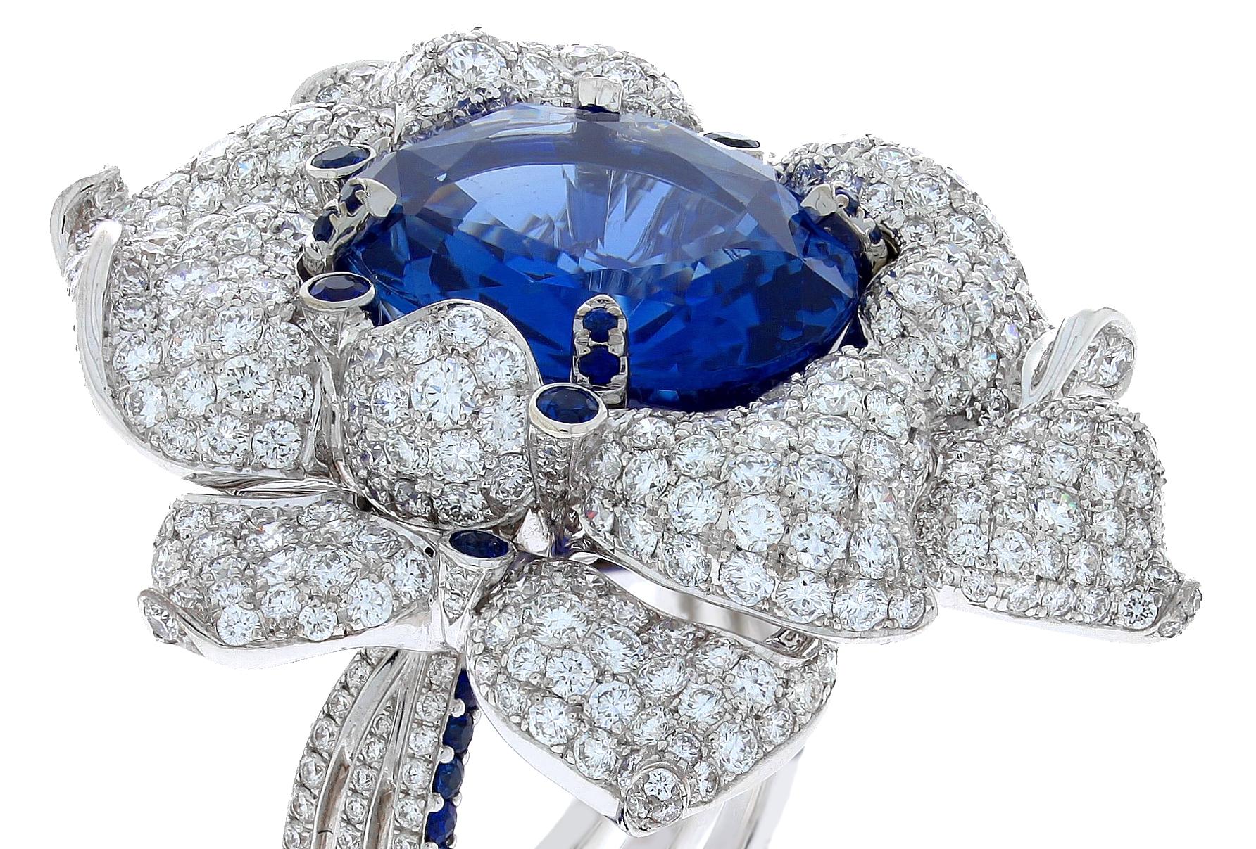 This mesmerizing 18 carat white gold transparent blue oval sapphire and diamond ring by Chatila features 49 smaller sapphires spread out on a bed of white diamonds on the petals. The band is also decorated with three rows of diamonds and a front row