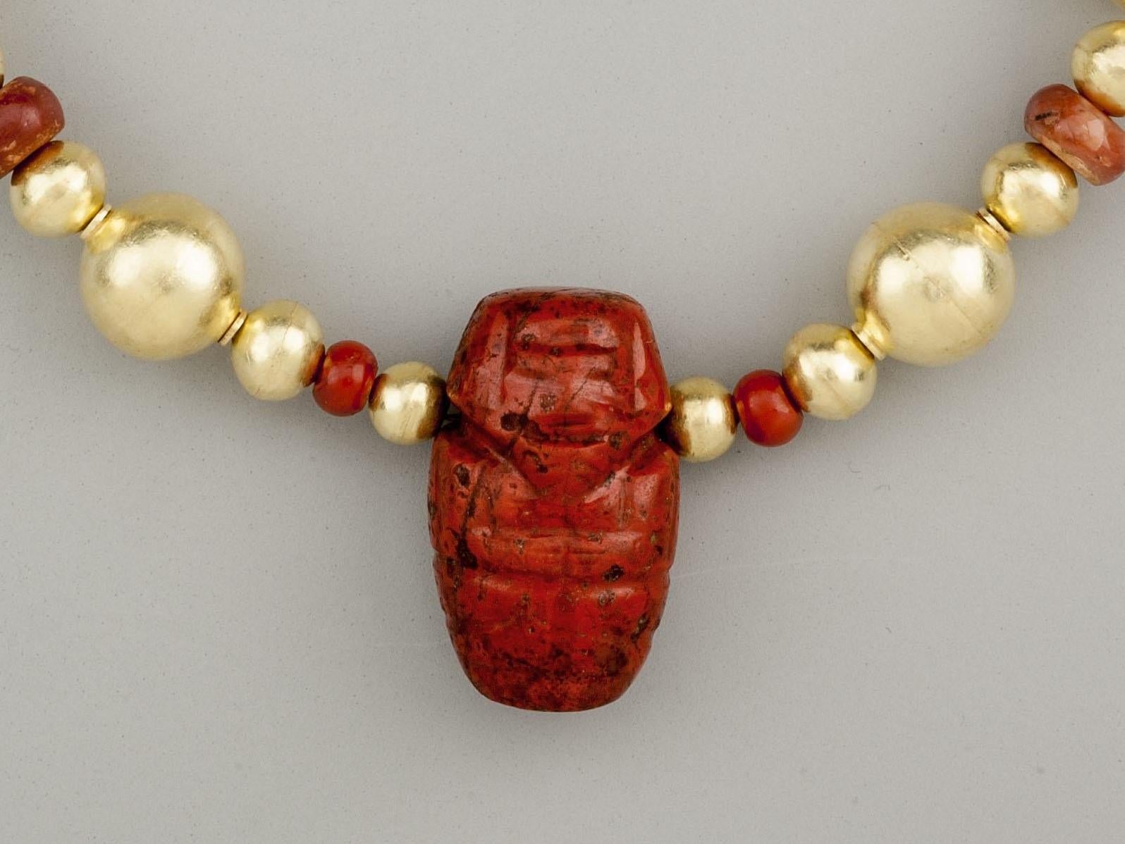 Twenty-eight round gold beads with ten carnelian beads, two of which are cylindrical tubes and eight flattened spheres, and a jasper effigy of a man, presumably a chief. The stone pieces are said to be from the Tairona people of Colombia, South
