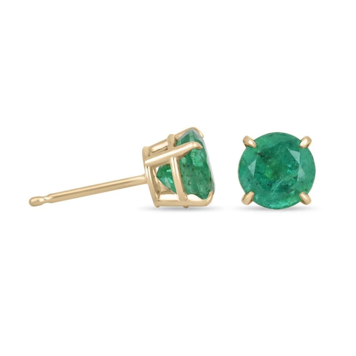 Featured here is a stunning set of round Zambian emerald studs in fine 14K gold. Displayed are rare, rich dark forest green emeralds with good transparency, accented by a hand-crafted four-prong gold mount, allowing for the emerald to be shown in