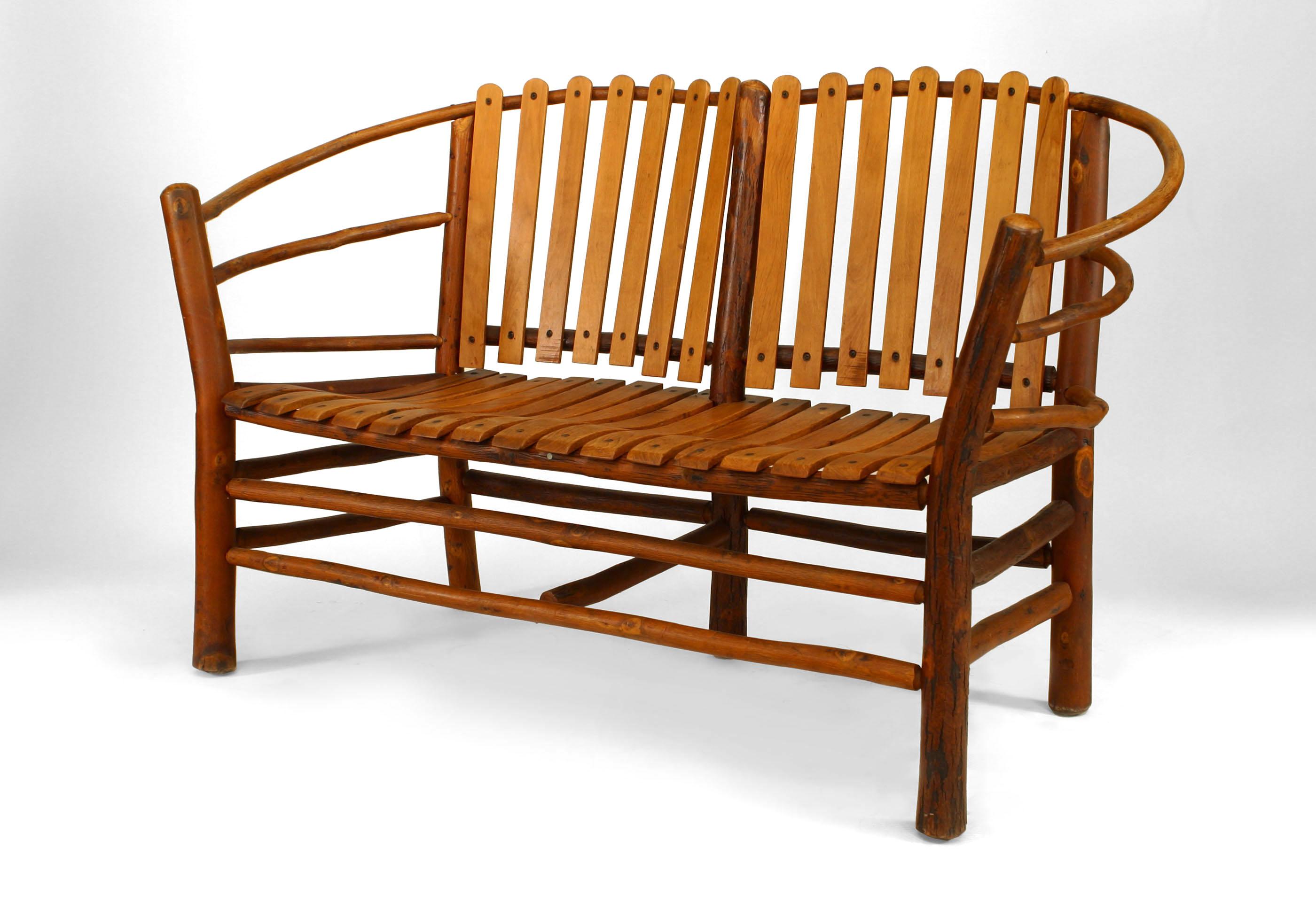 Bearing the brand of the Old Hickory Company of Martinsville, Indiana, this rustic loveseat is composed of oak with slat design seats, bowed arms, and a parallel bar stretcher joining four legs.