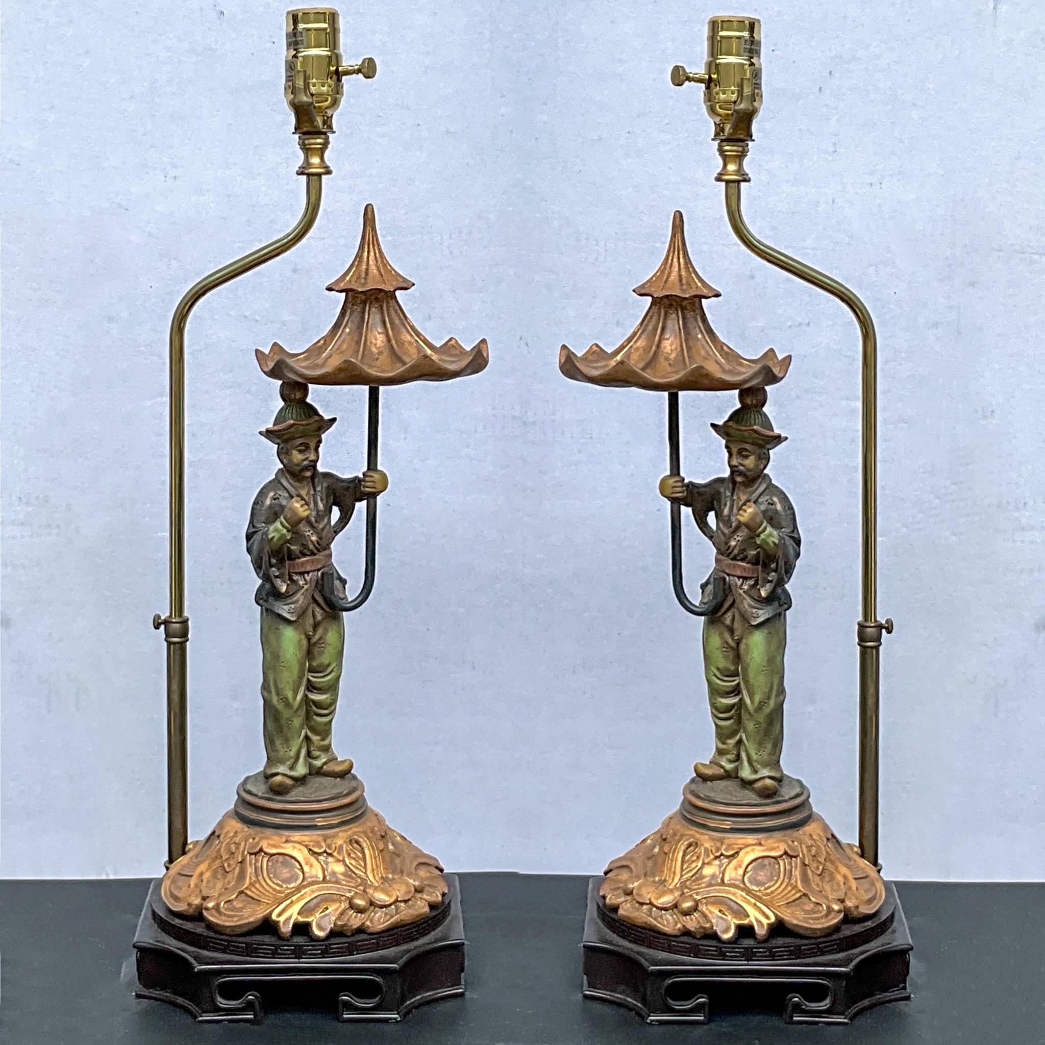 This is a lovely pair of chinoiserie table lamps attributed to Chelsea House. They depict a single Asian male holding a gilded pagoda from umbrella. The brass shade support is adjustable.  The height to the umbrella is 18 inches. 