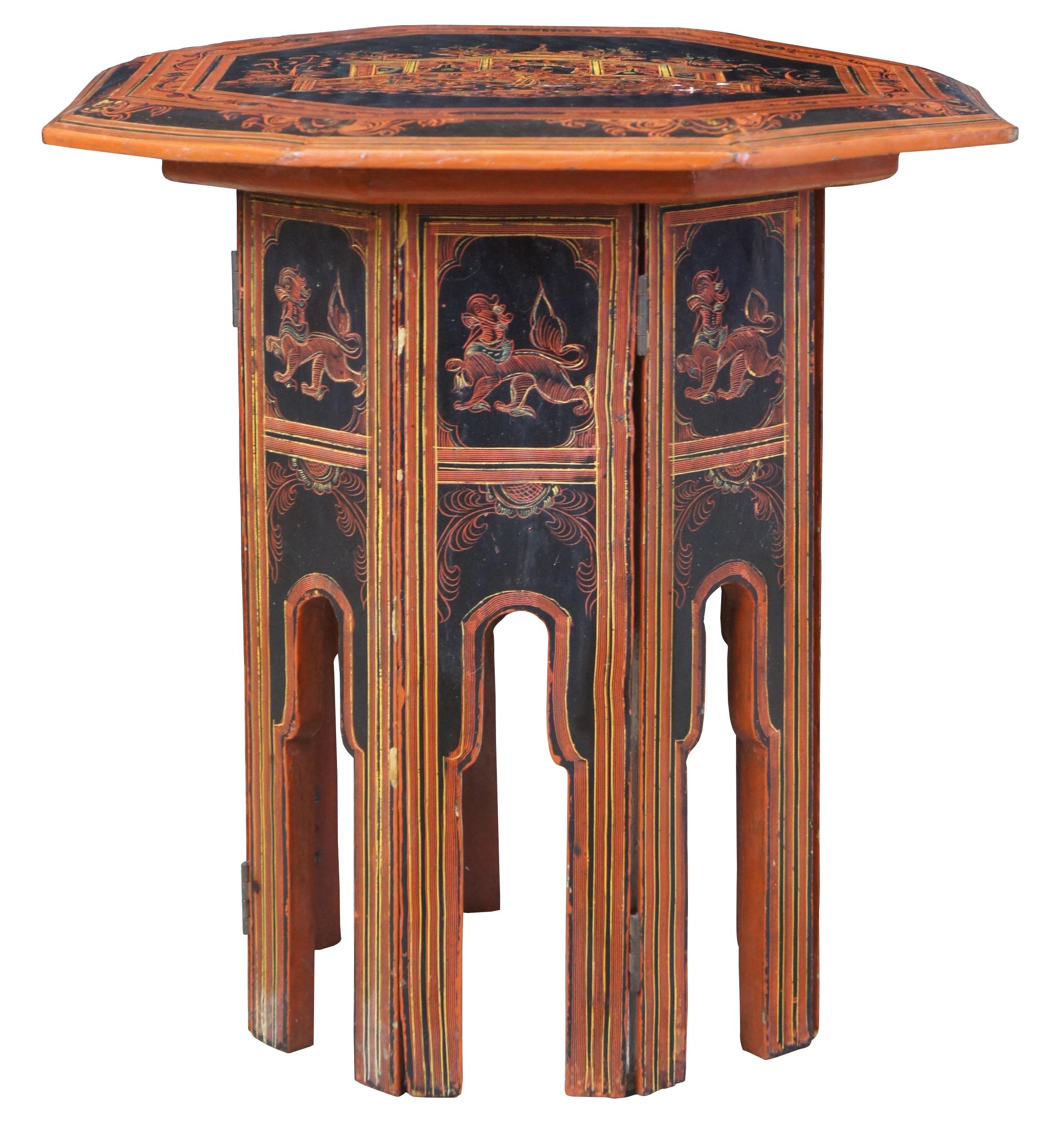 Mid 20th Century Burmese folding table. Red & Black lacquer with octagonal top and arched panelled base. Features a ceremonial temple scene along the top with 3 figures seated on cushions within a fenced area. Includes vivid floral motif and figural