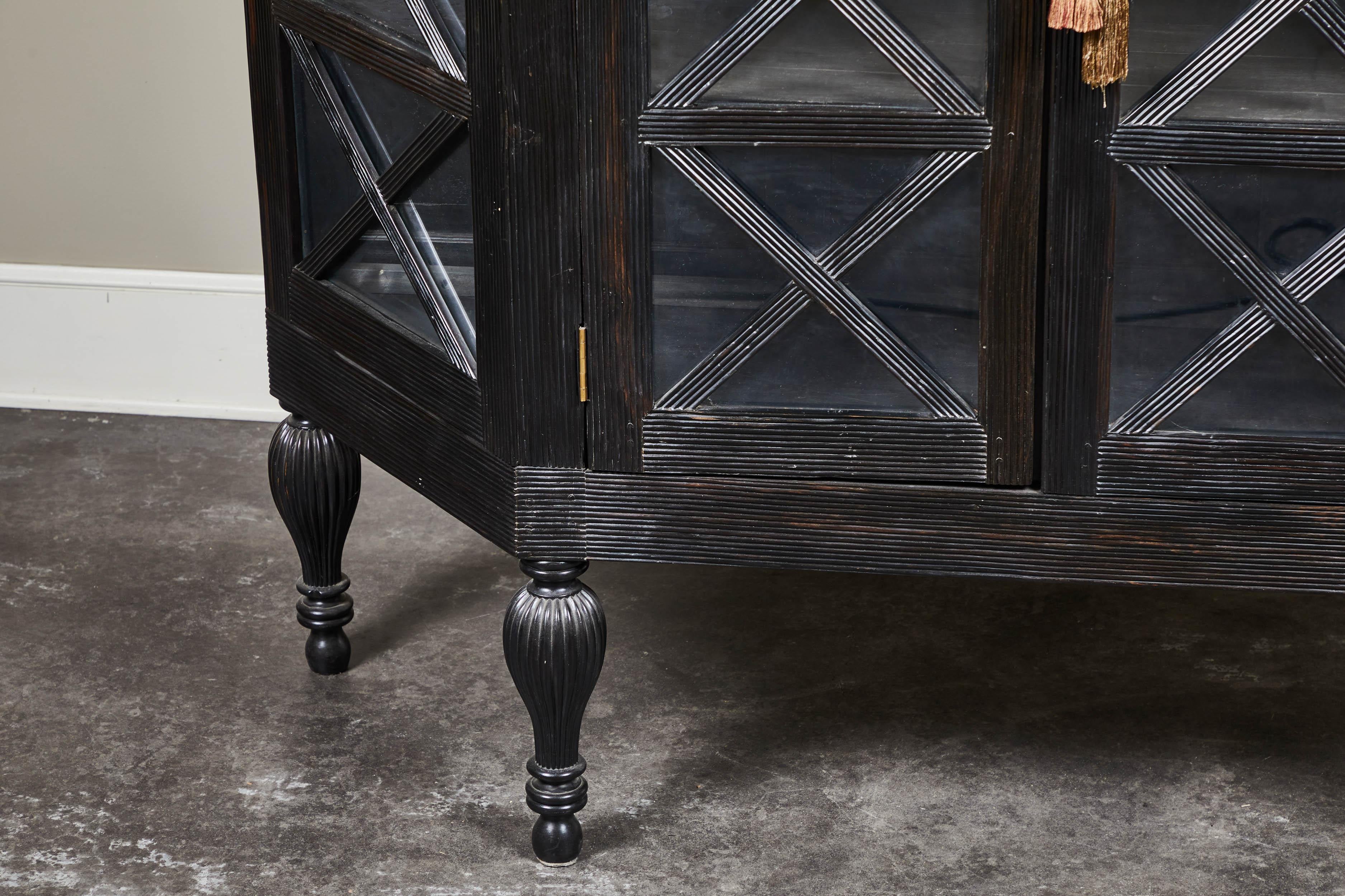 A 20th century British Colonial solid ebony two-door display cabinet, from Sri Lanka.