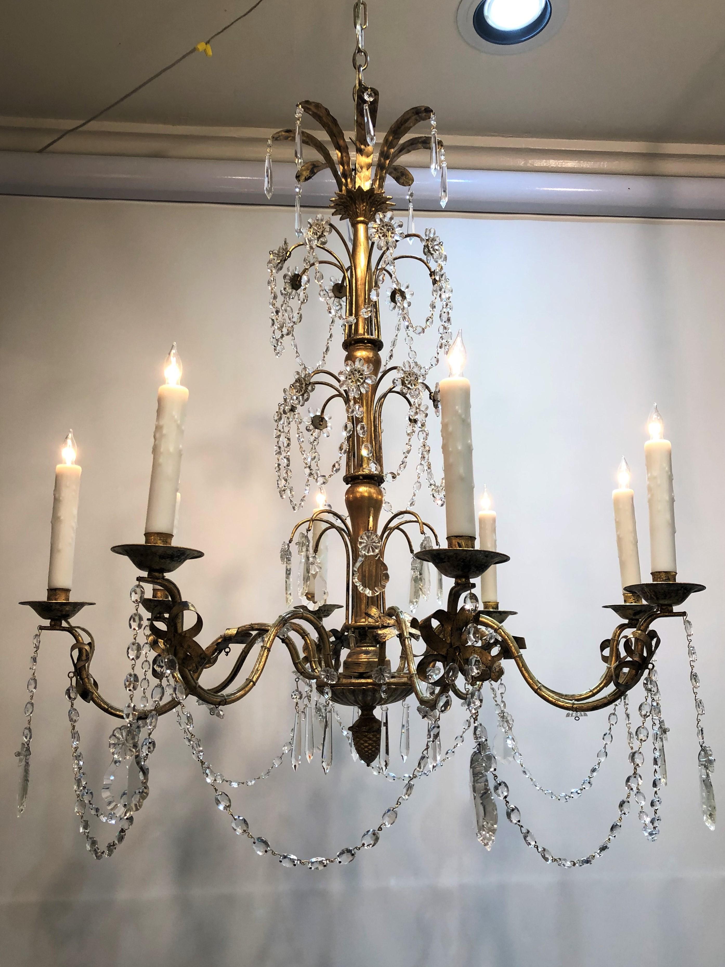 This chandelier was made in France during the mid-20th century. The body is tole with eight candle arms with crystal prisms and swags beneath each bobeche. Featuring a stylized pine cone drop finial. The chandelier has recently been rewired with new