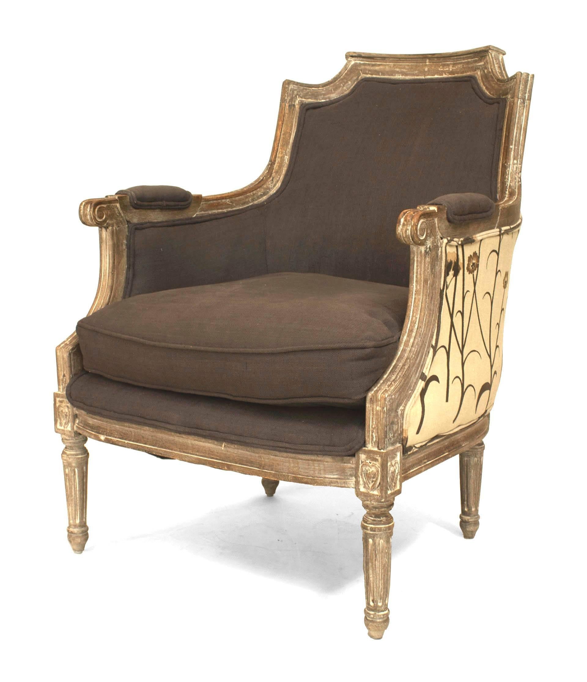 Twentieth century French Louis XVI style bleached bergere armchair with a shaped back pediment and classicizing carvings at the arms and legs. The chair is upholstered in floral fabric at the exterior and dark grey fabric at the seat, back, and