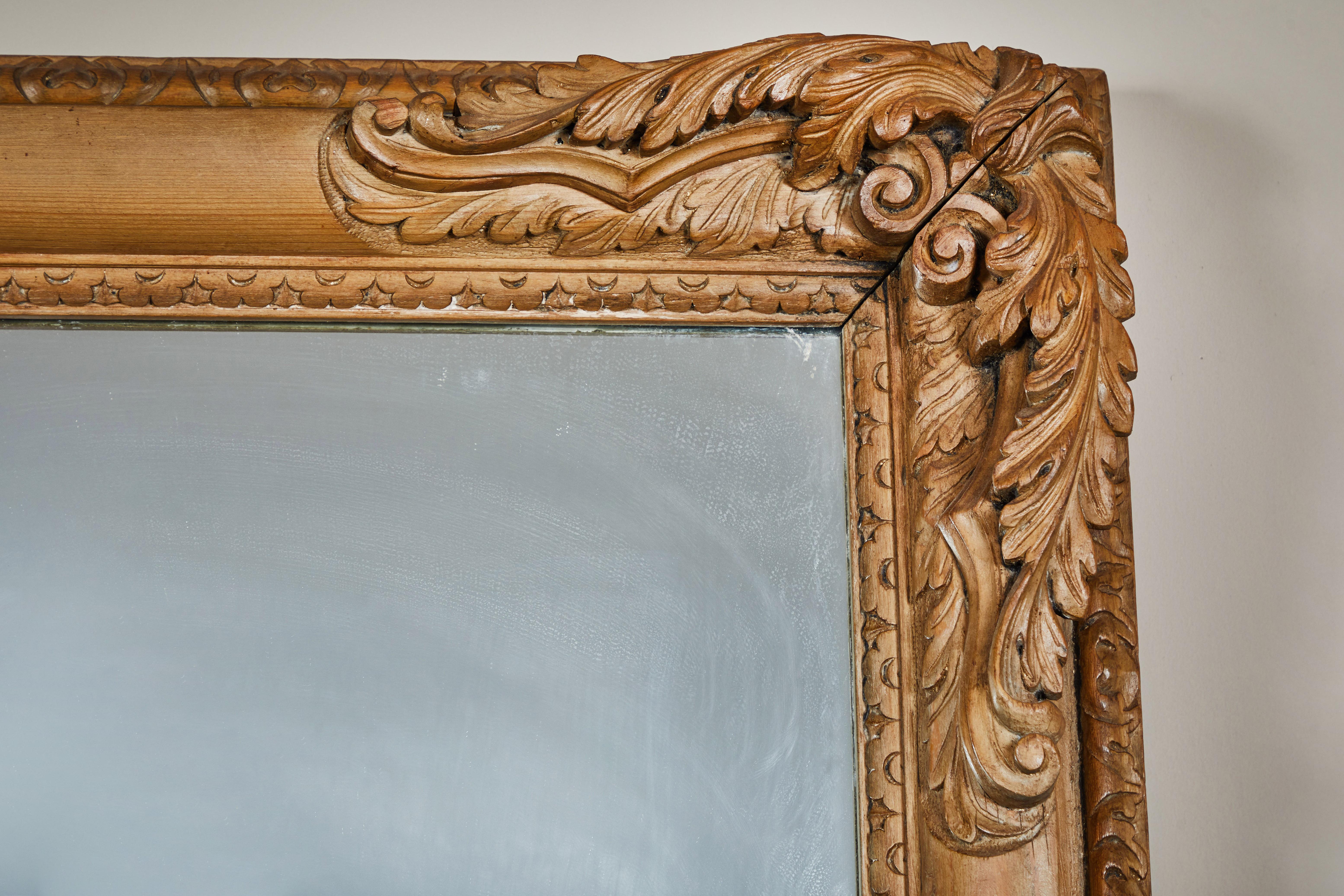 Grand miroir encadré de bois clair avec des coins fortement sculptés. Miroir de grande taille, incliné vers le sol, ou installé en position basse dans un hall d'entrée, un dressing, etc.