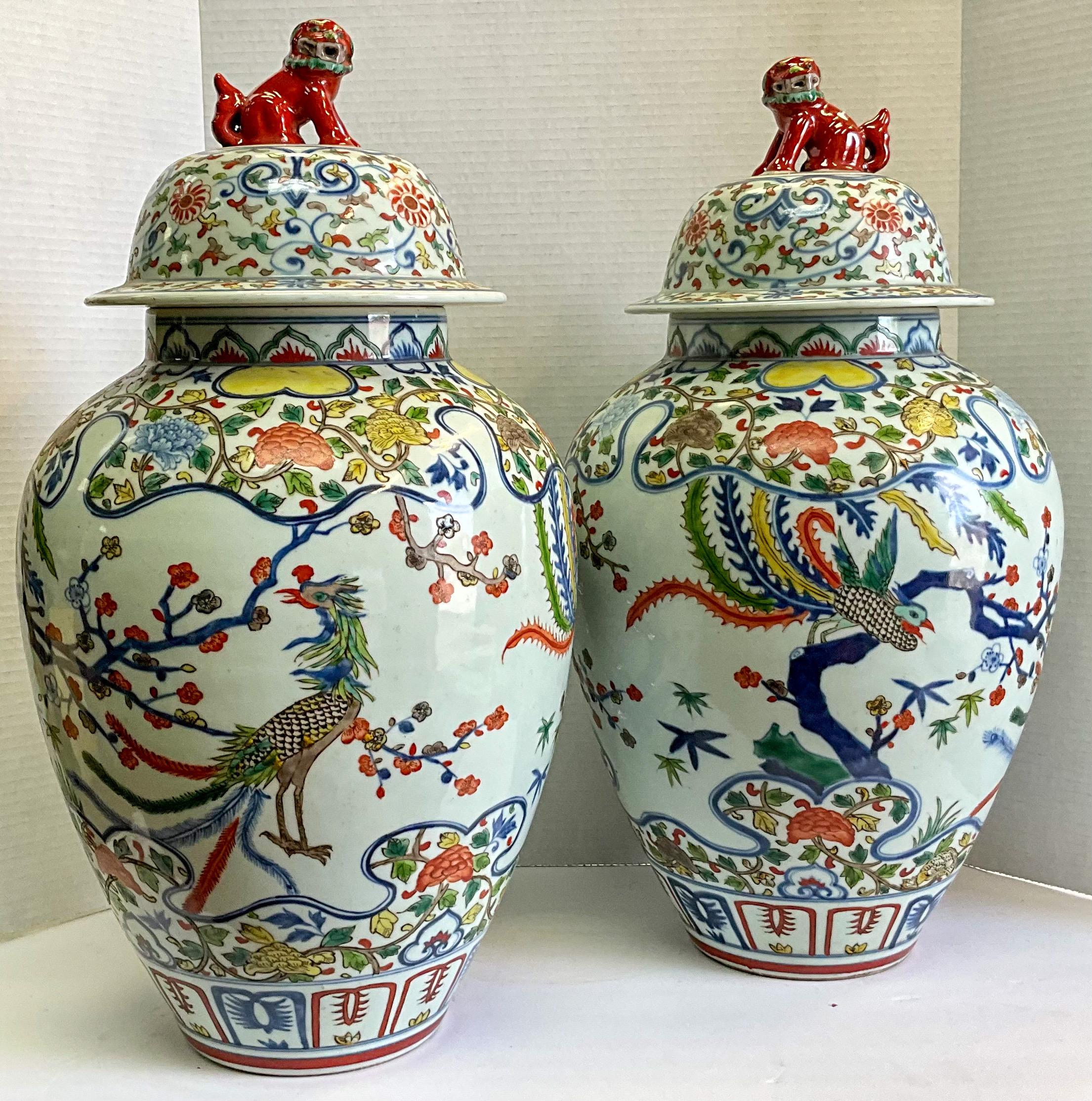 This is a pair of large scale Chinese ginger jars with vivid bird motifs and bright coral foo dog finials. The birds appear to be some sort of pheasant. The colors really make them quite unique. They are marked.