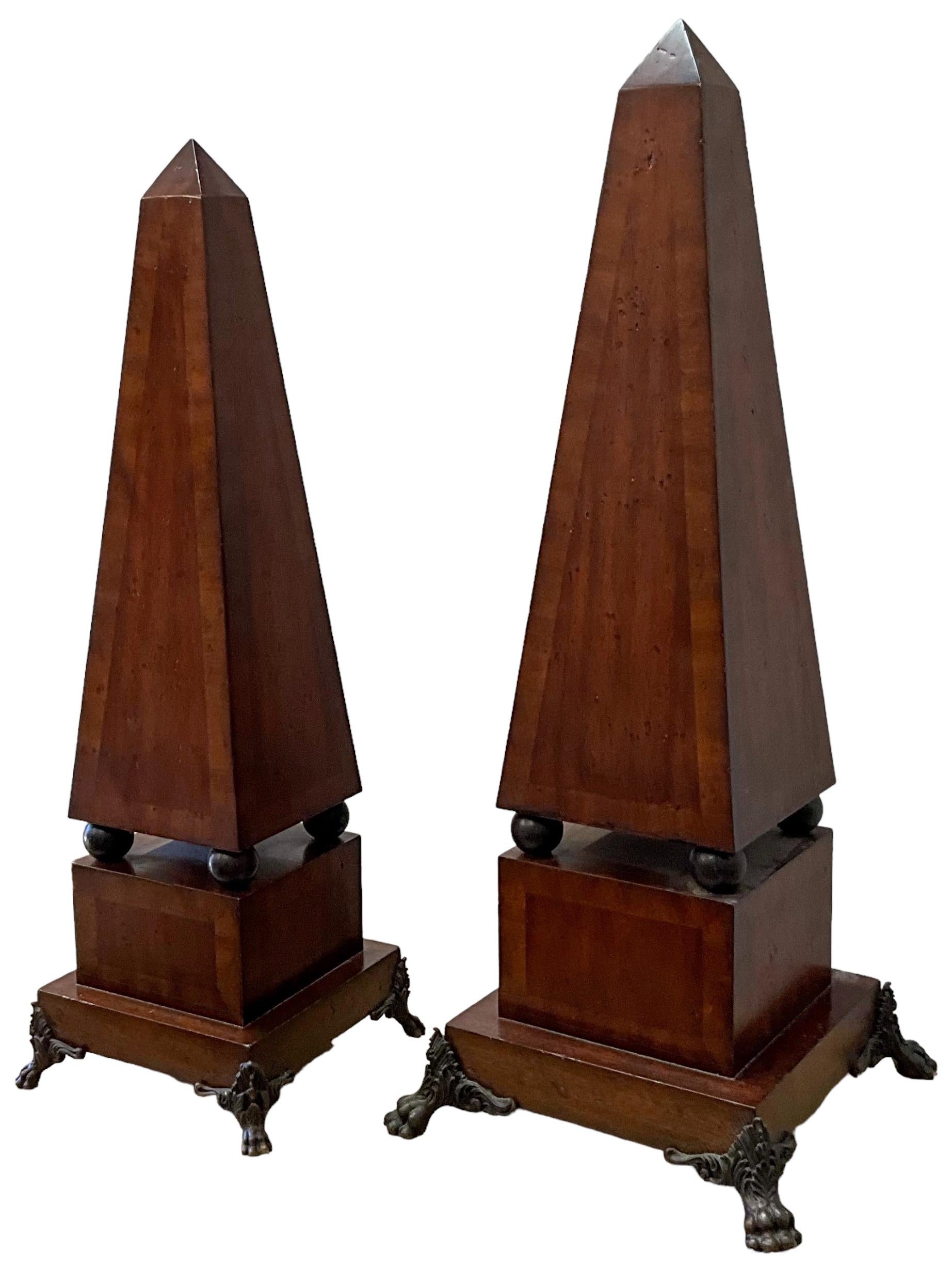 This is a set of neo-classical style banded mahogany obelisks with patinated bronze paw form feet. They are unmarked. The smaller is 7.75” square and 23.5” in height. 