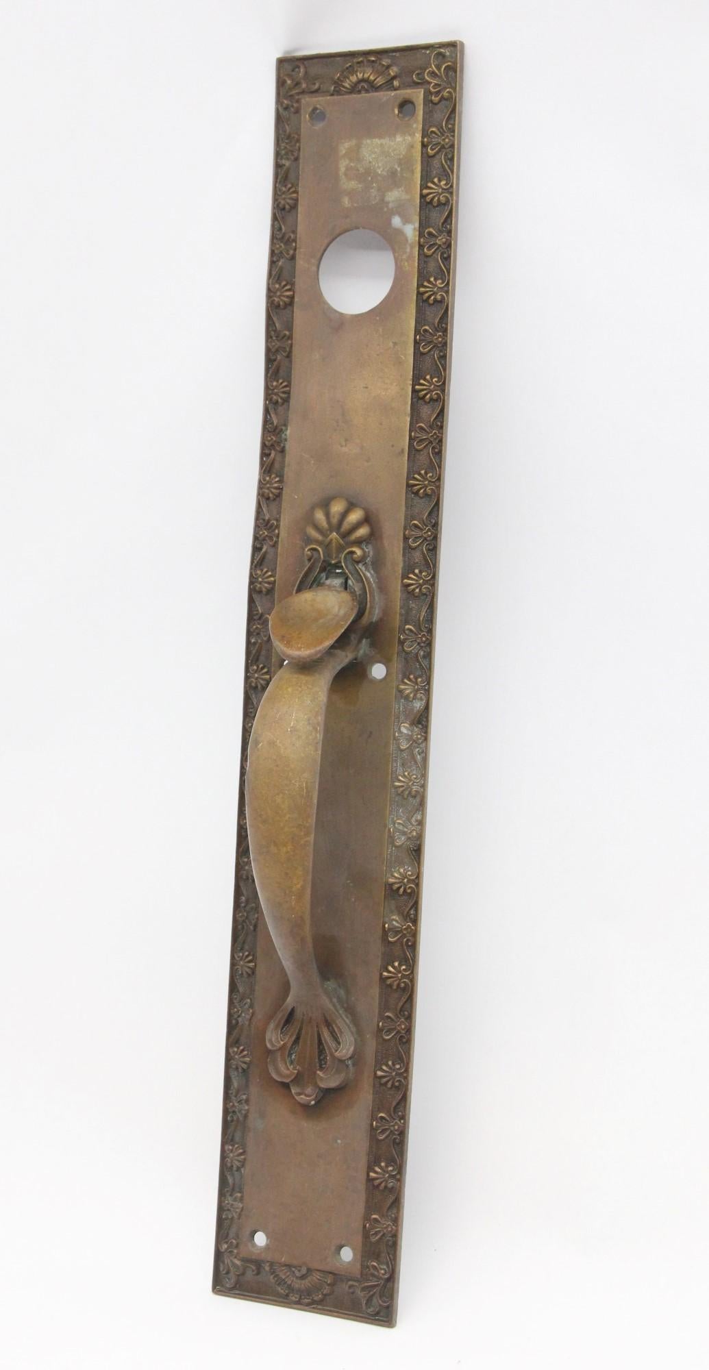 20th Century Neoclassical style bronze door pull featuring a flower and shell design. This piece includes a thumb latch and lock insert. Please note the plate is slightly bent. One available. This can be seen at our 400 Gilligan St location in