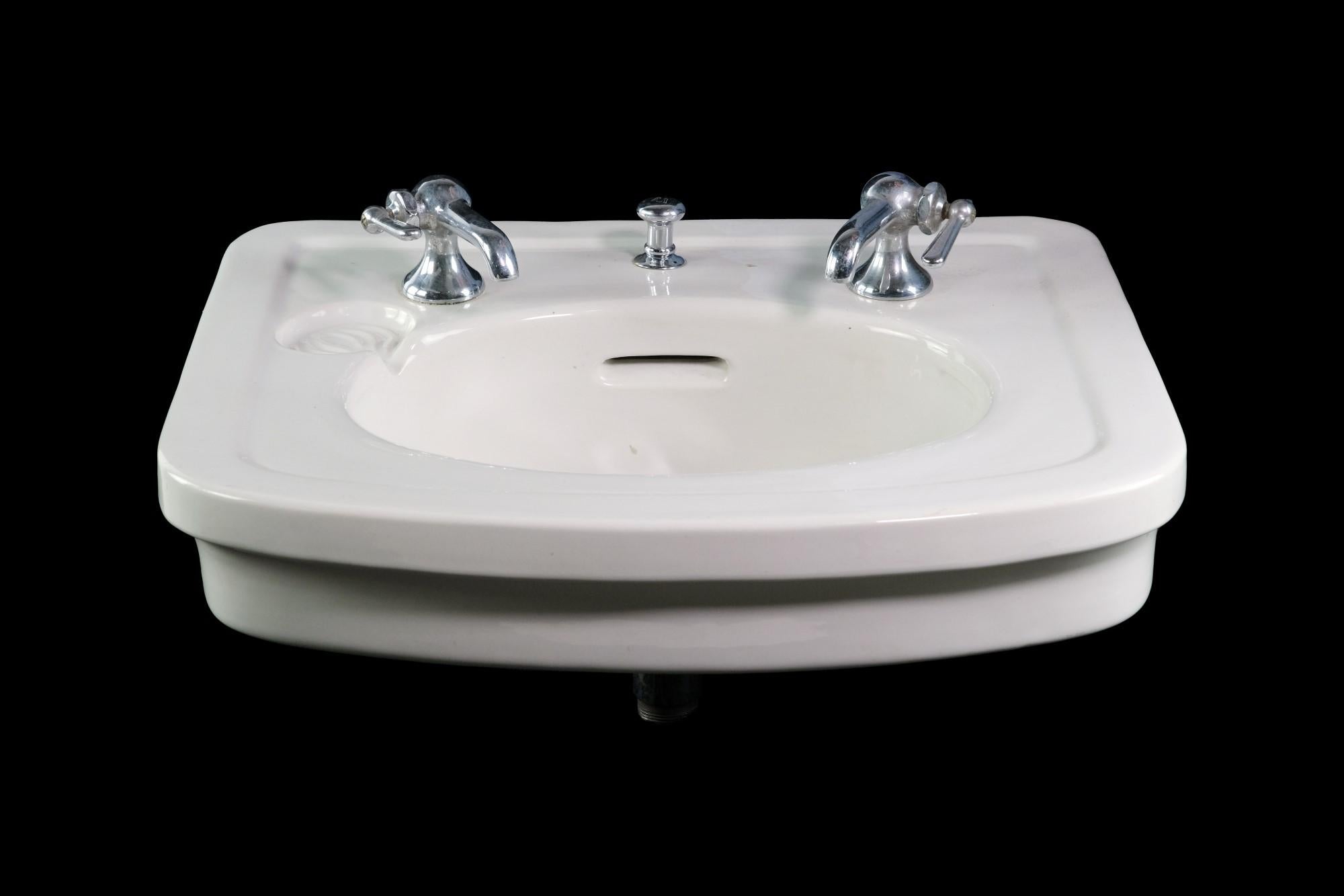 20th Century white ceramic wall mount sink with an oval basin. Oval front design. Features nickel hardware. This can be seen at our 400 Gilligan St location in Scranton, PA.