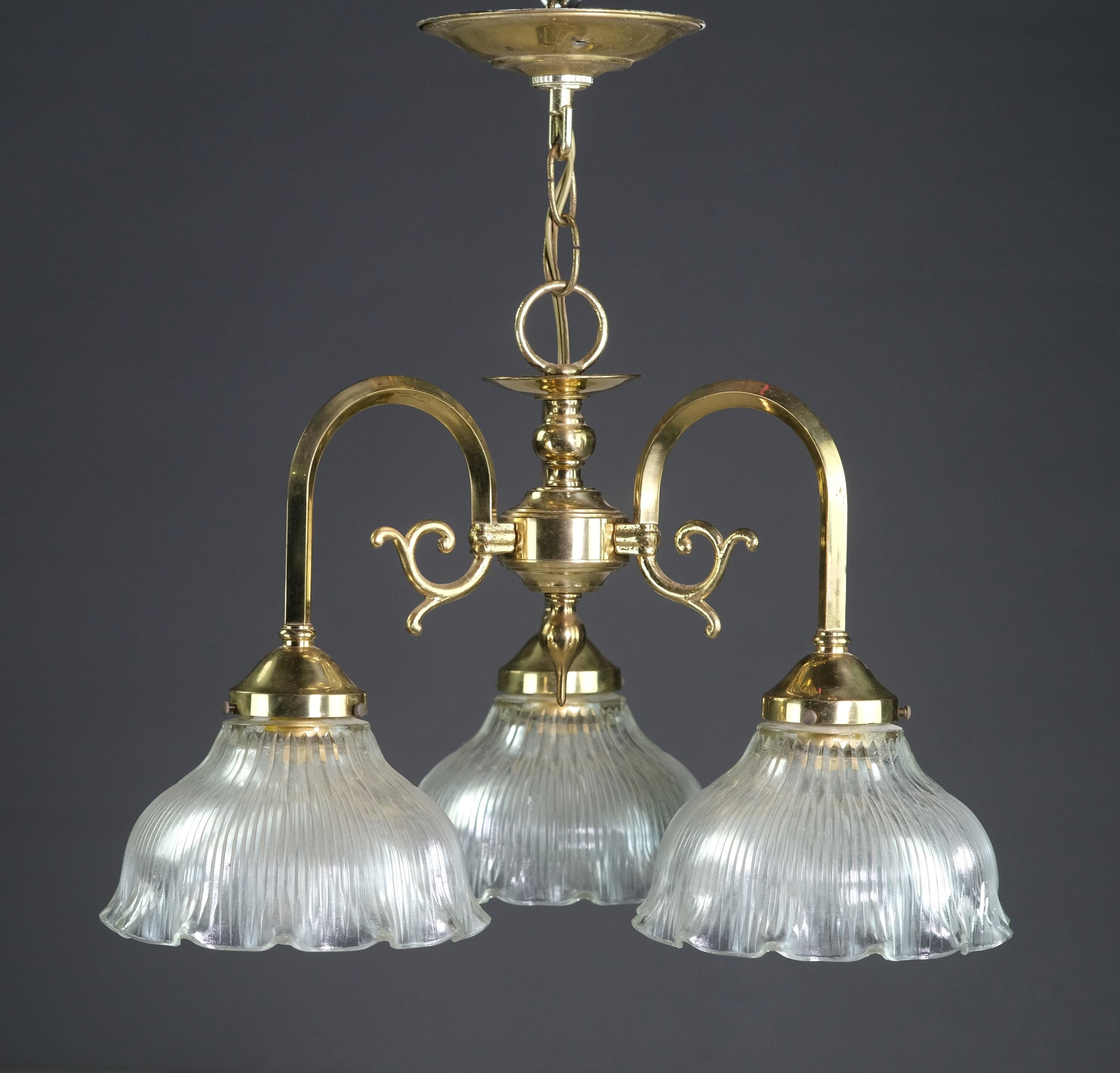 Polished brass three arm down light chandelier with clear fluted and ruffled glass shades. 20th Century pendant light done in polished brass. Features 3 Holophane tulip style ribbed shades. Takes 3 standard medium base lightbulbs. Cleaned and