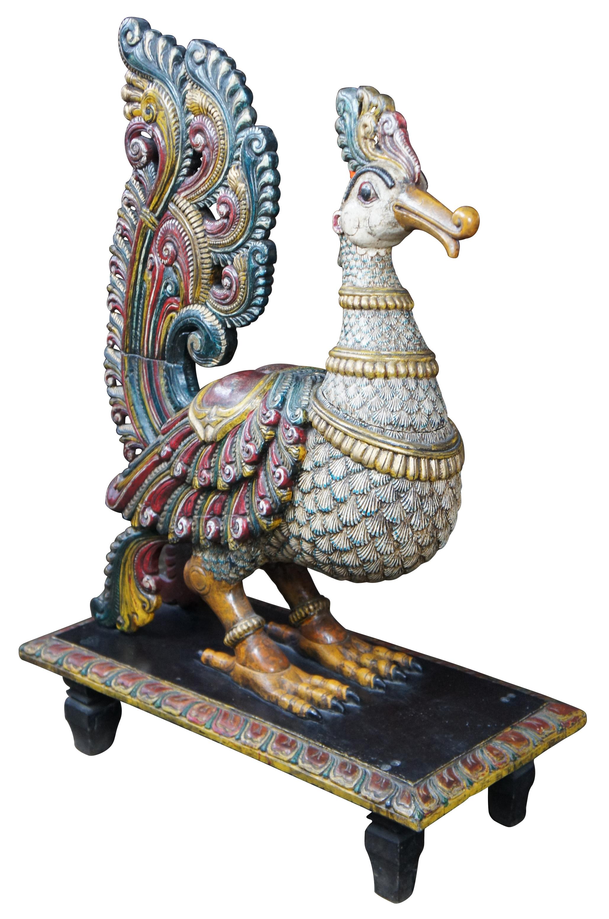 20th century South Indian carved and painted peacock statue. A Folk Art sculpture hand carved on a plinth base. Features bright colors of yellow, green, red and orange. A large sculpture with an eye catching presence on a floor, table or outcove.