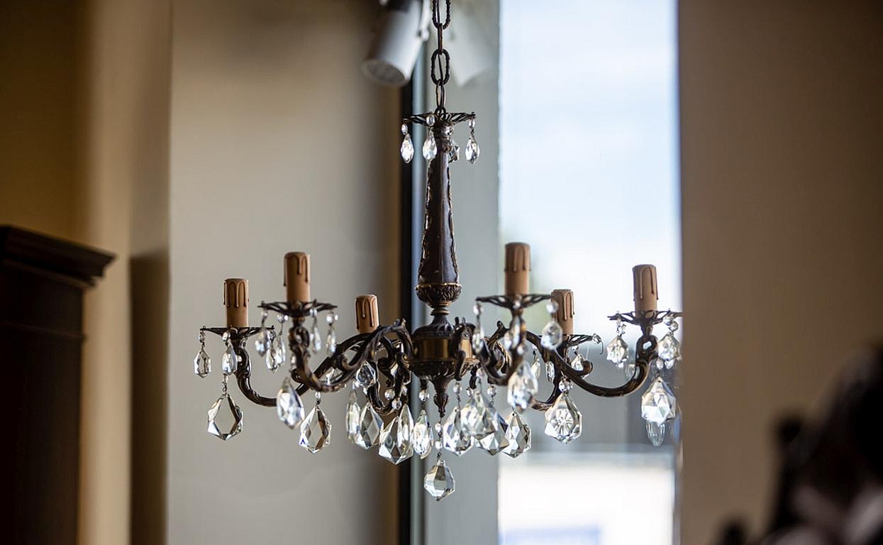 We present you this six-arm brass chandelier with hanging crystal elements.
It was manufactured before 1939.
There are sockets for six E27 light bulbs.
The power source is 230 V.

The chandelier is in very good condition. Three crystals are