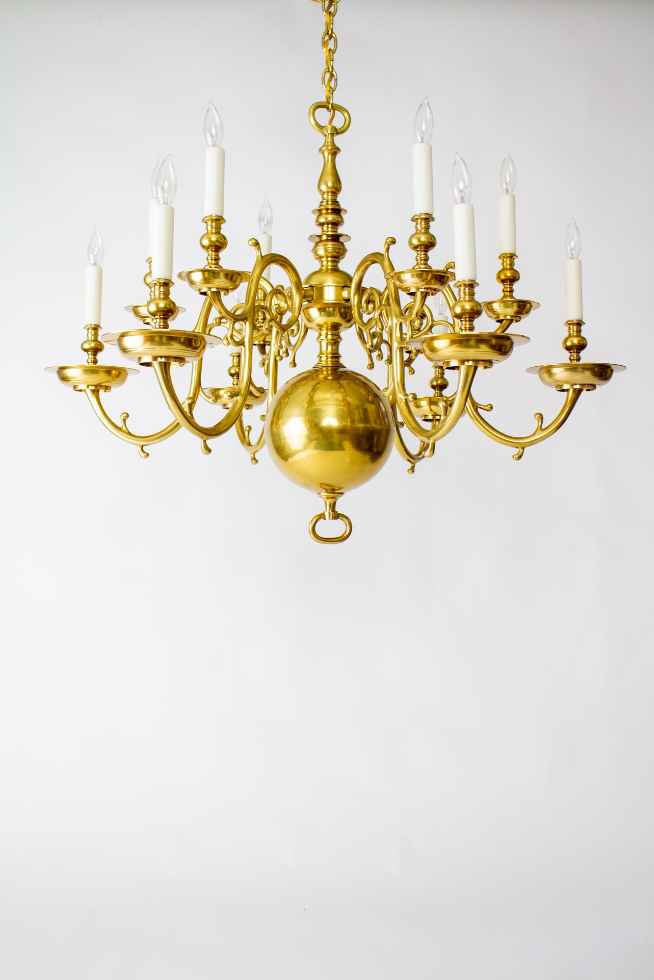 20th Century 12 arm Dutch colonial brass chandelier. Heavy cast brass chandelier, traditional style. Turned brass stem with a large brass bottom ball. Cast brass arms with turned brass candle cups. Two tiers, Six arms in the top tier and six on the