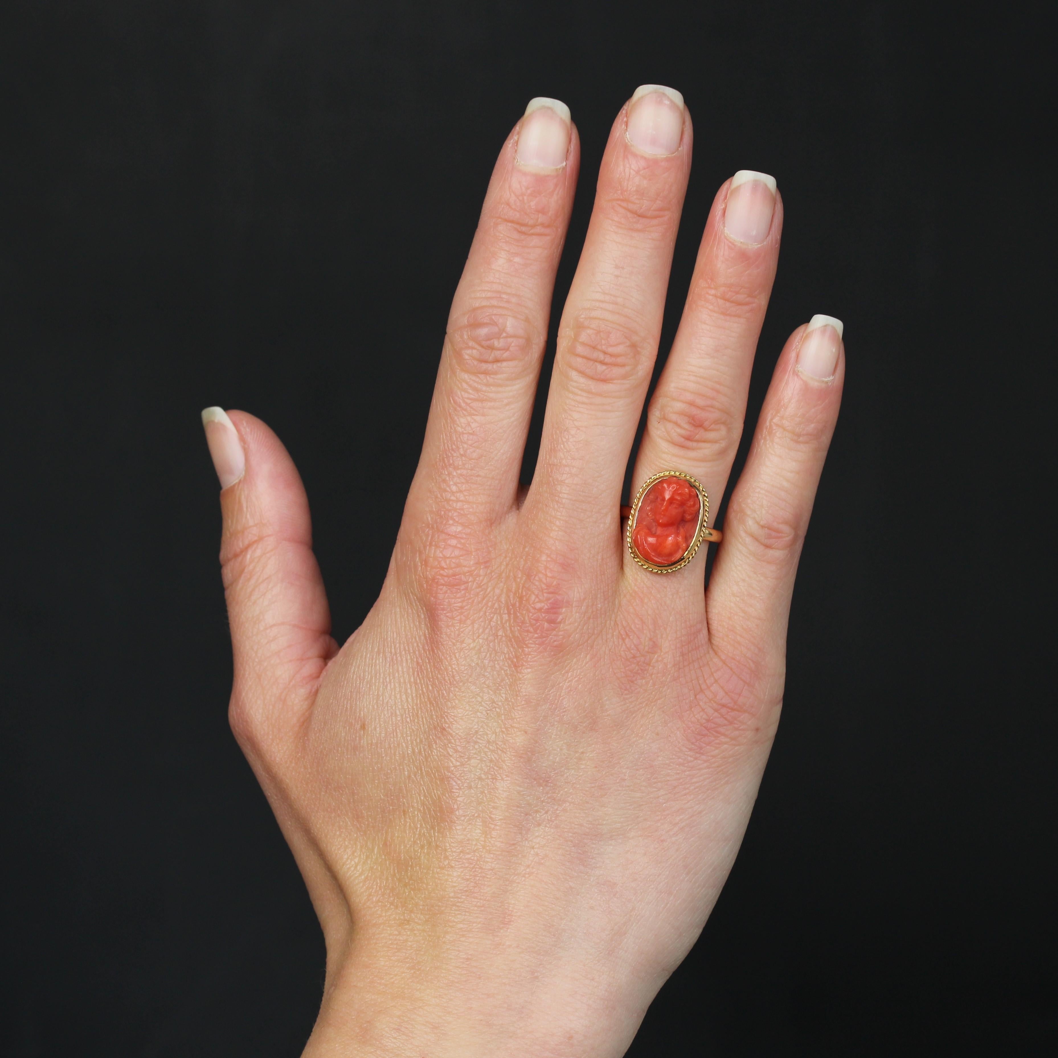 Bague en or jaune 18 carats.
Cette bague ancienne présente un anneau bombé en or jaune supportant un motif ovale orné d'un cordon d'or. Un camée sur corail représentant une jeune femme est serti au centre. Une gravure est présente à l'intérieur de